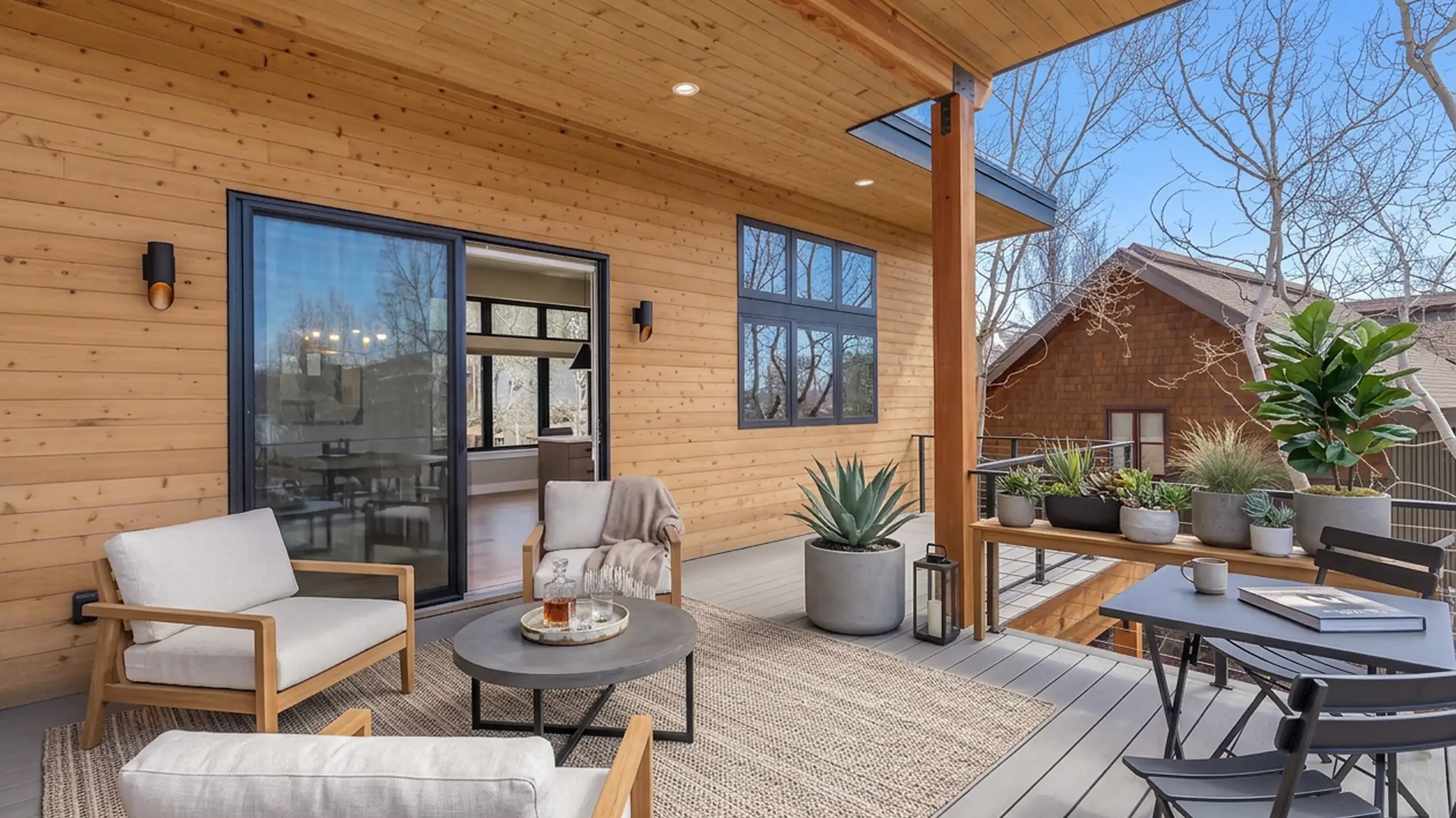 Telemark covered deck with cedar siding, white outdoor lounge chairs, potted plants, cable railing, and sliding glass door to interior