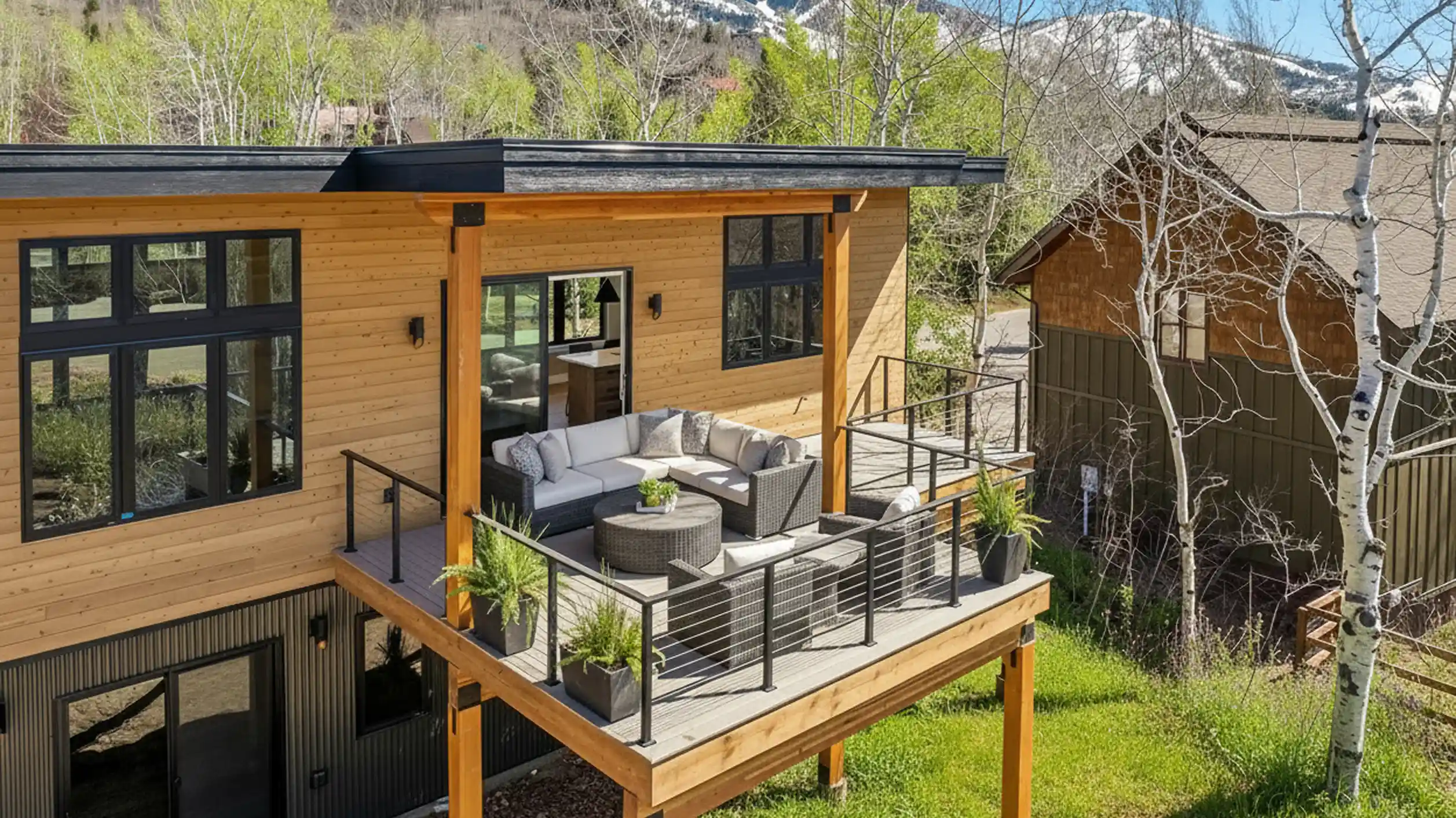 Telemark elevated upper deck with gray wicker sectional sofa and coffee table, cable railing, cedar siding, and mountain and aspen tree views
