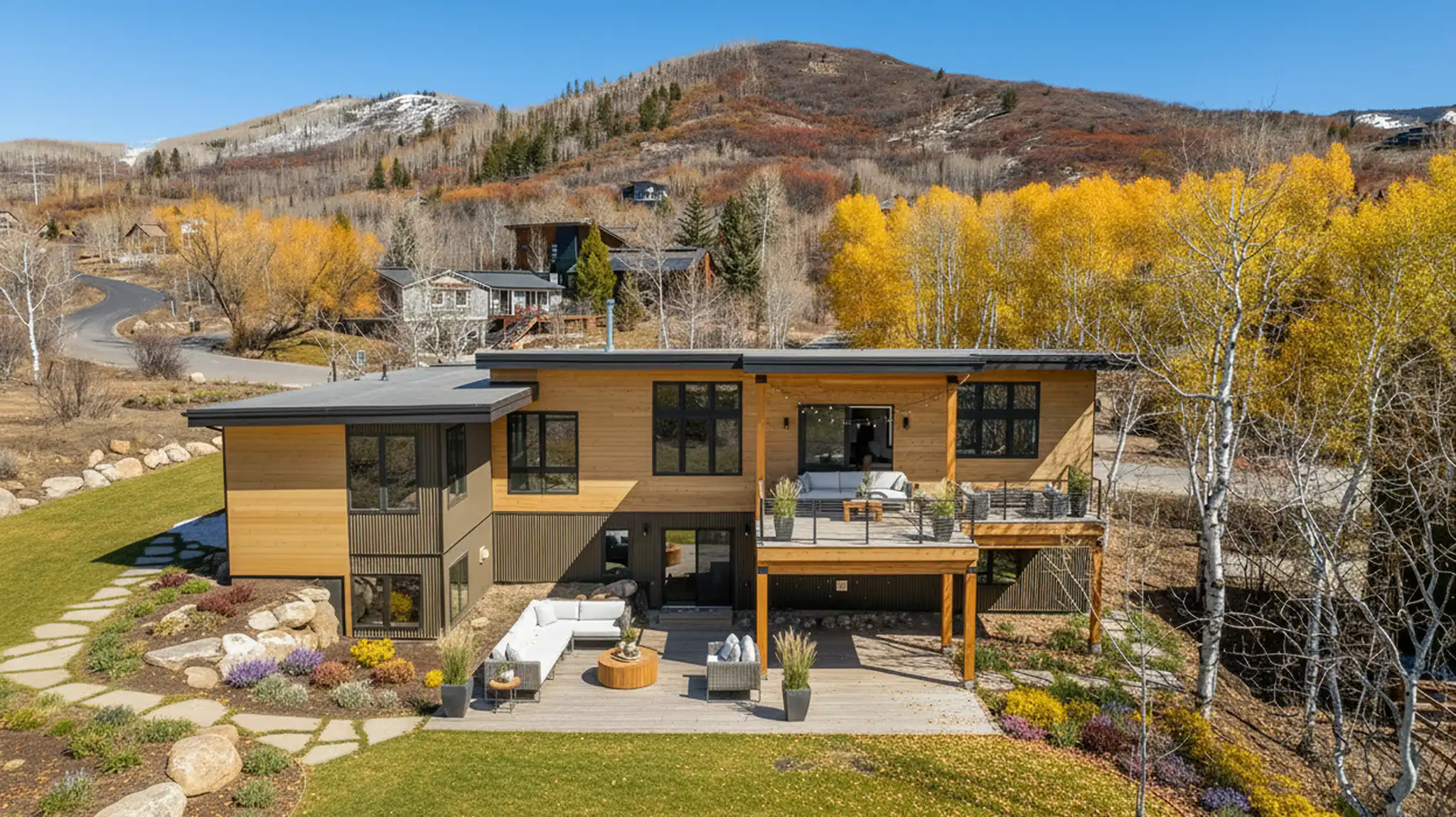 Telemark aerial exterior view of two-story home with warm cedar siding, flat roof, upper deck with furniture, fall foliage, and mountain backdrop