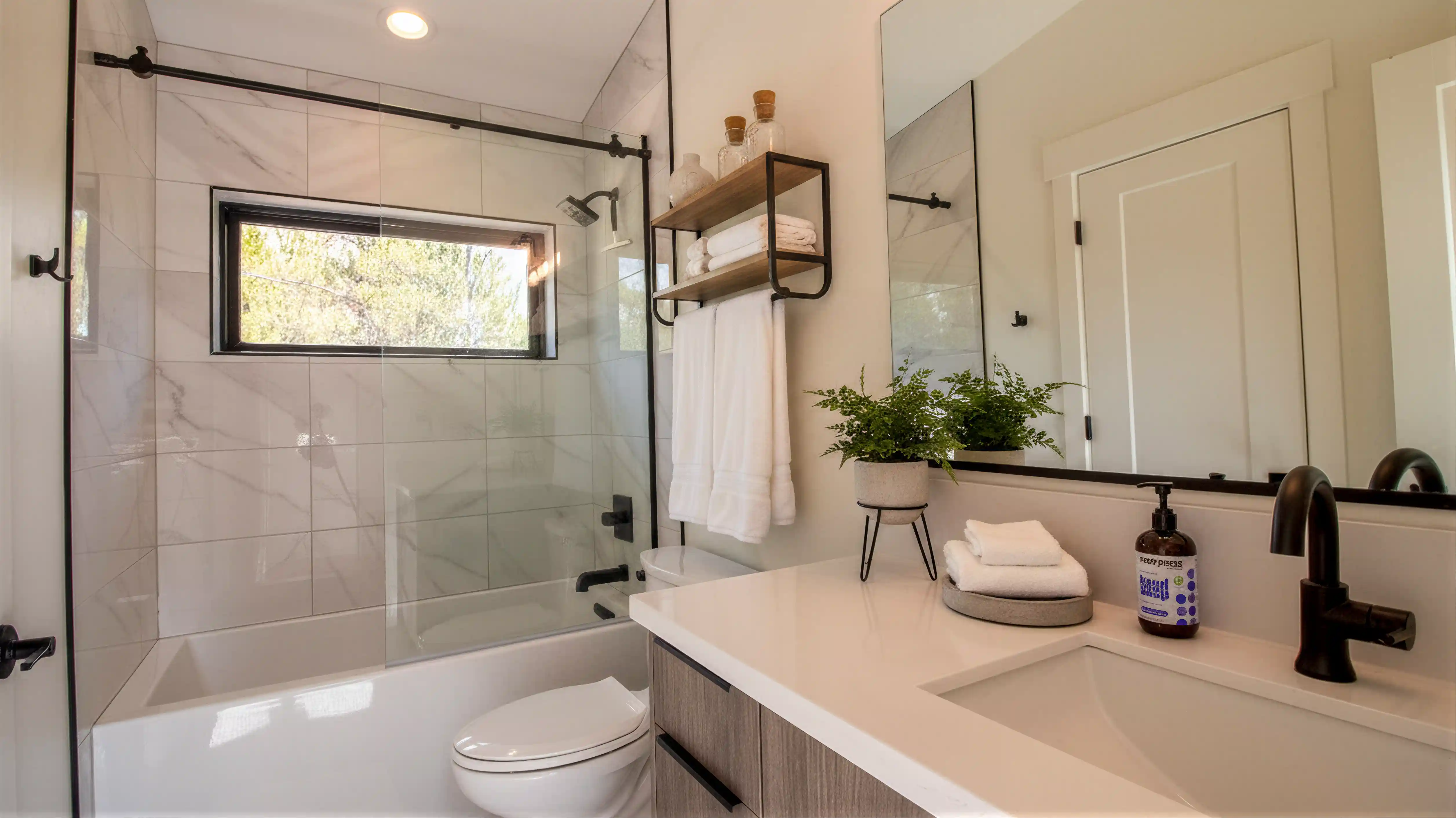 Hideaway secondary bathroom with white quartz vanity, matte black fixtures, floating shelf, and glass tub-shower combo with marble tile