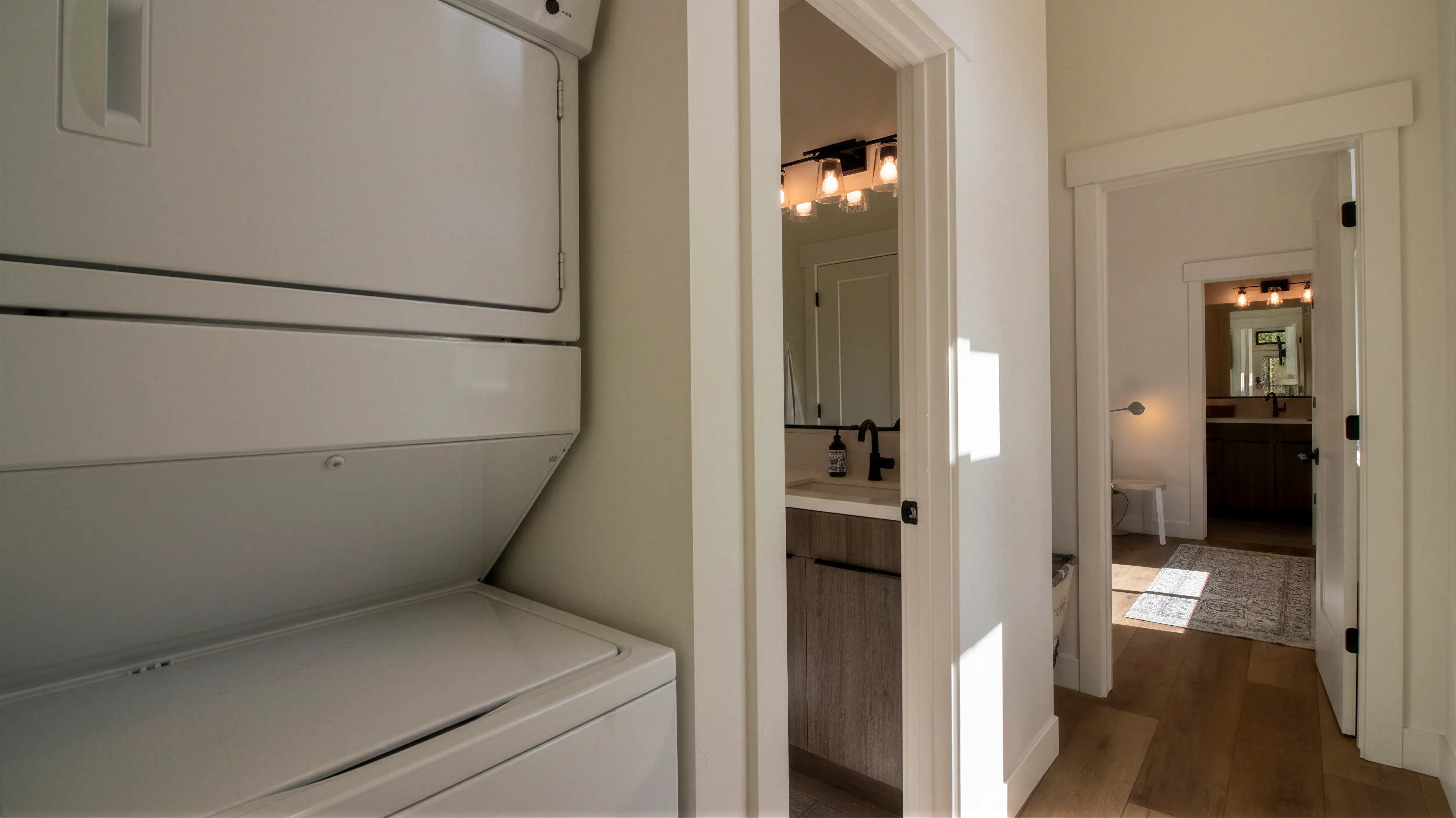 Hideaway hallway with stacked washer and dryer, open doorway to lit bathroom with vanity, and second doorway to bedroom