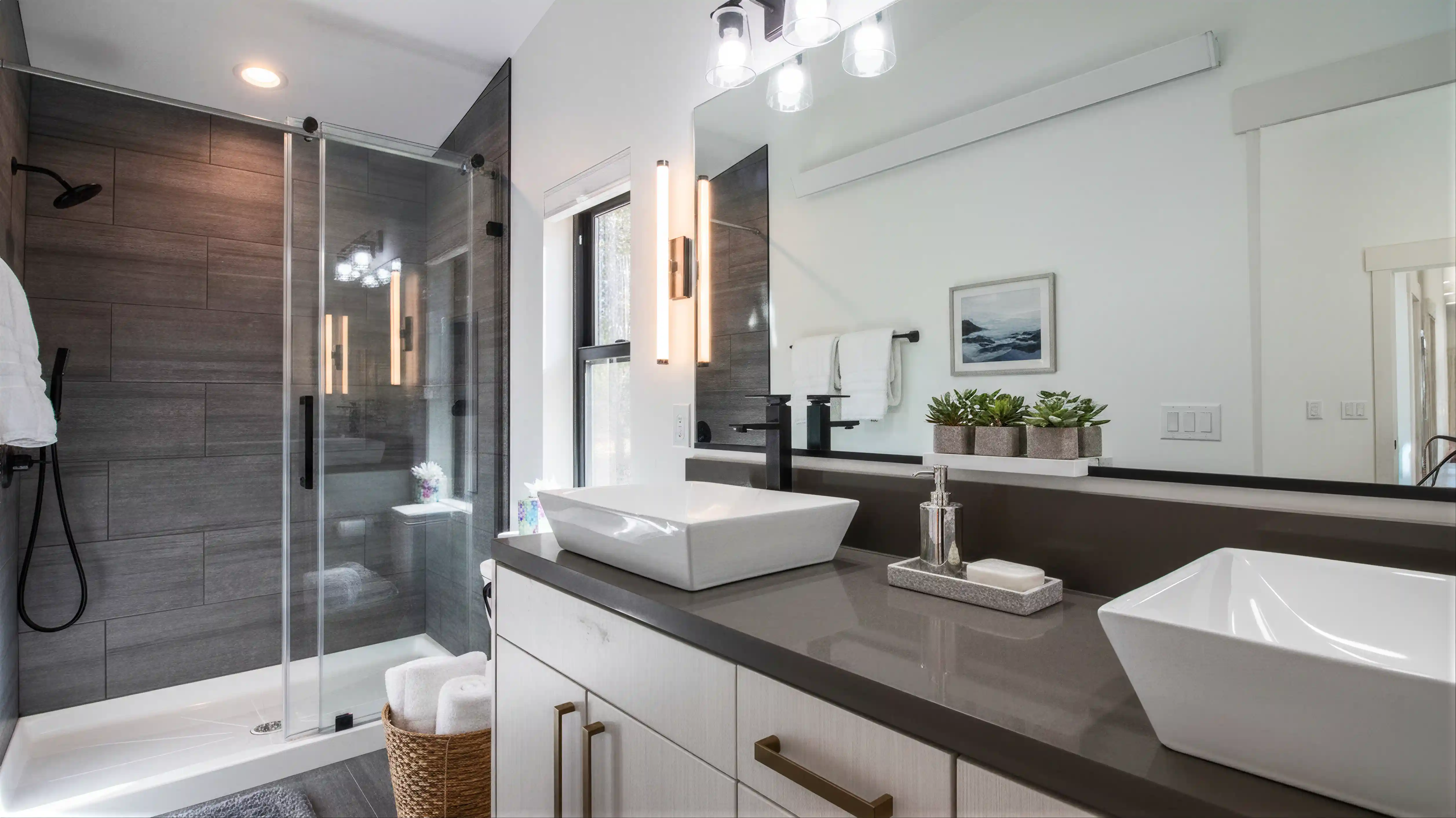 Hideaway primary bathroom with double vessel sinks on dark gray quartz vanity, white cabinetry, brushed gold fixtures, and glass shower with dark gray tile