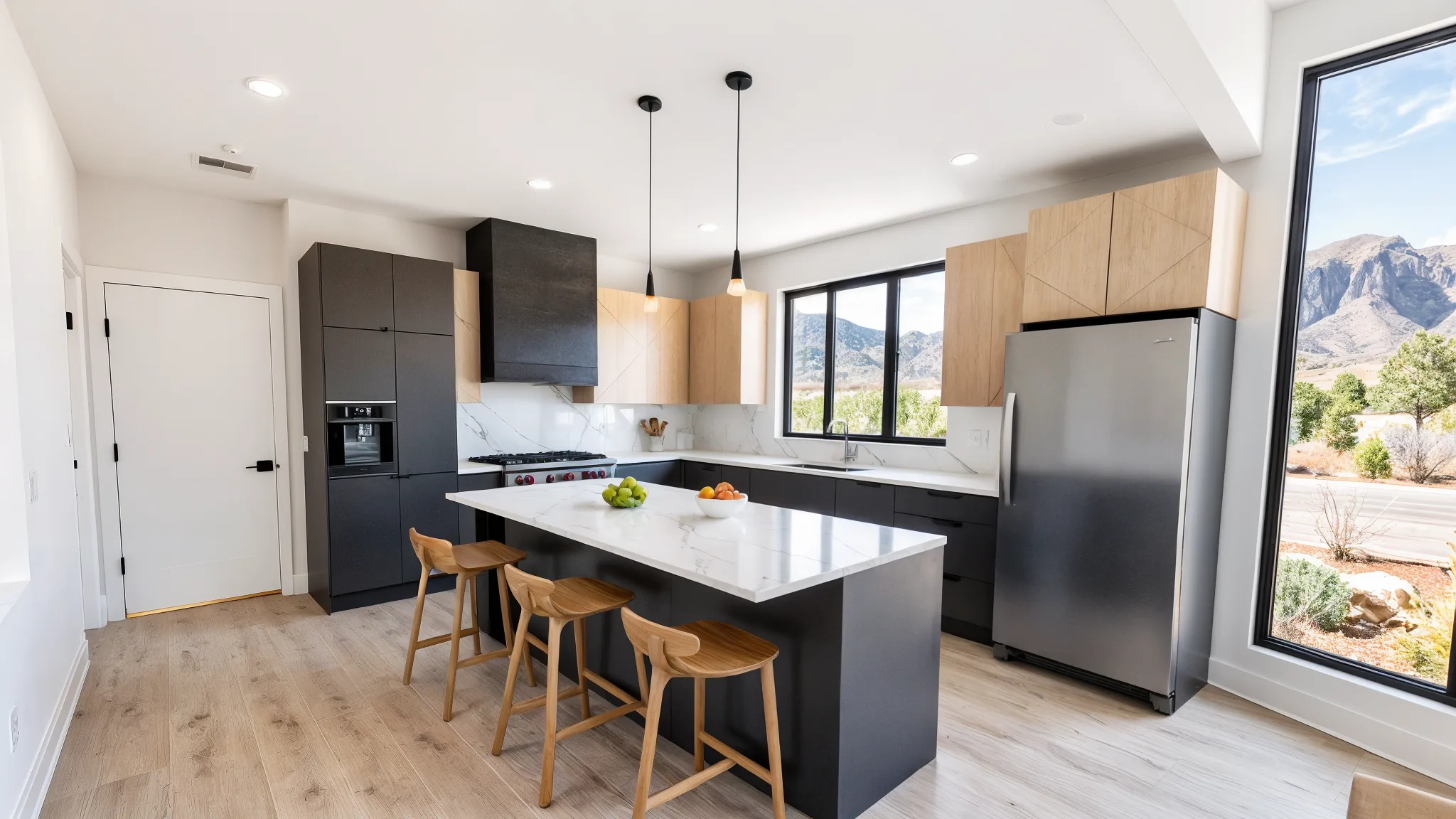 Modern kitchen with dark charcoal lower cabinets, light wood upper cabinets, white quartz island with bar stools, black pendant lights, and large window with mountain views