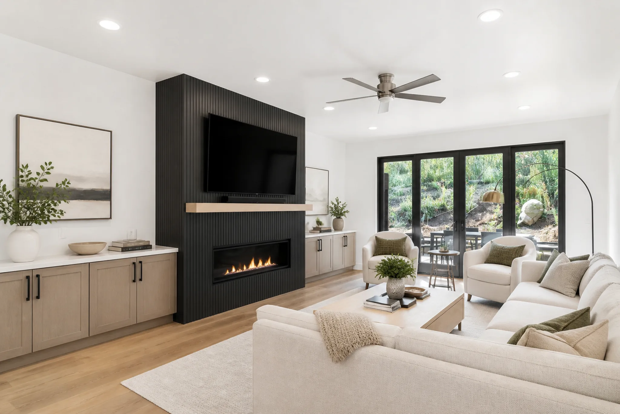 Modern living room with cream curved sofa, black fluted fireplace surround with wall-mounted TV, ceiling fan, and glass sliding doors to outdoor patio