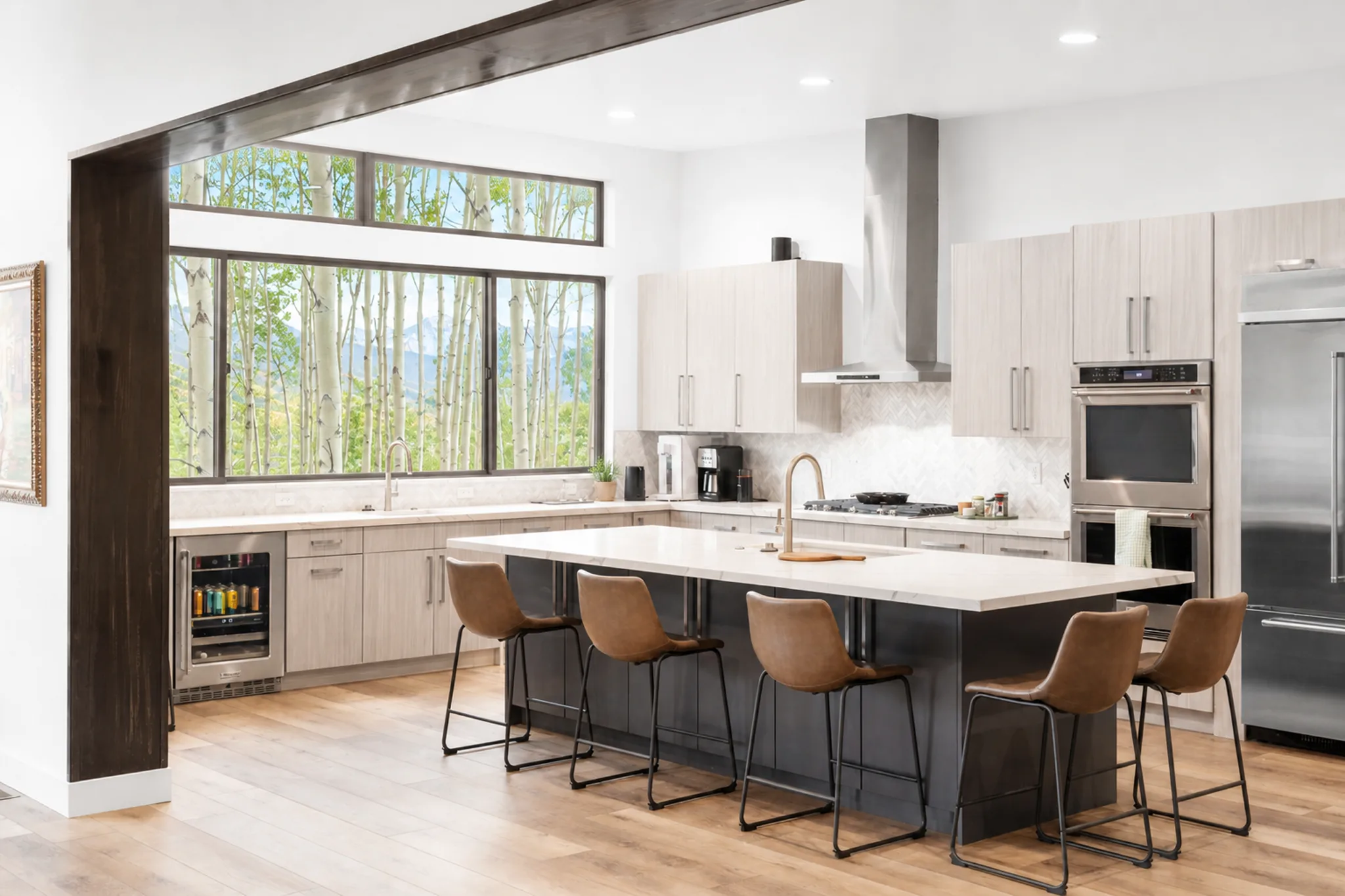 Open kitchen with large dark island, brown leather bar stools, light gray upper cabinetry with open shelving, stainless steel appliances, and windows with fall aspen tree views
