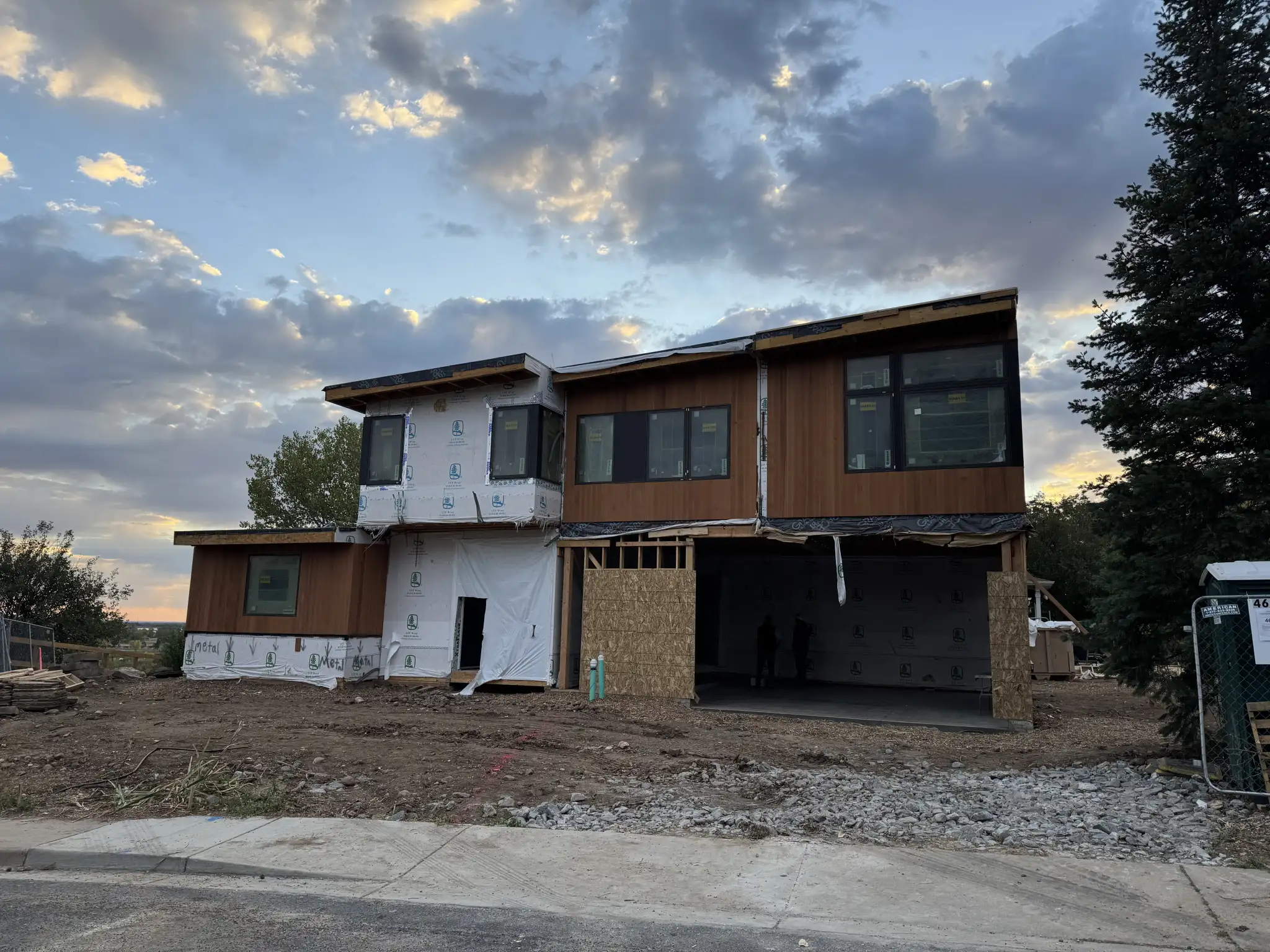 Two-story home under construction at dusk with wood and wrap siding, open garage bay, and dramatic cloudy sunset sky