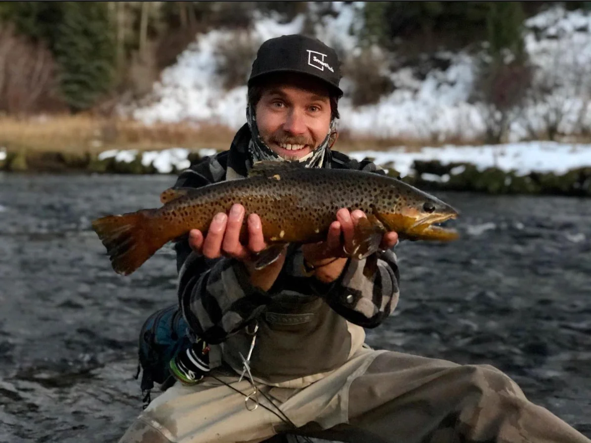 Smartpads team member fly fishing in a snowy river holding a large brown trout