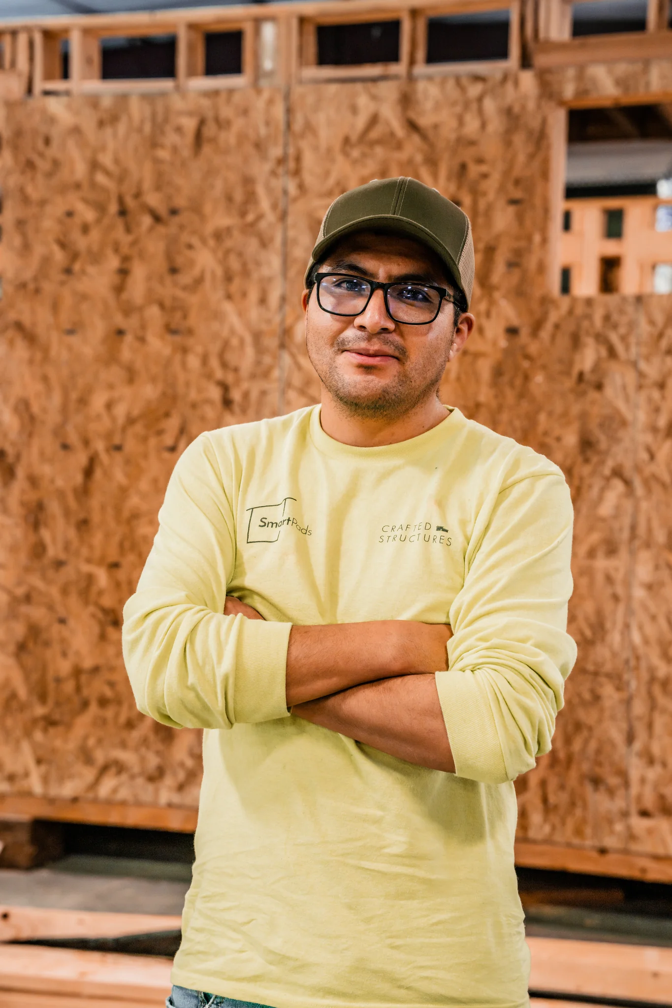 Smartpads team member wearing glasses and cap smiling in front of OSB panels in the factory