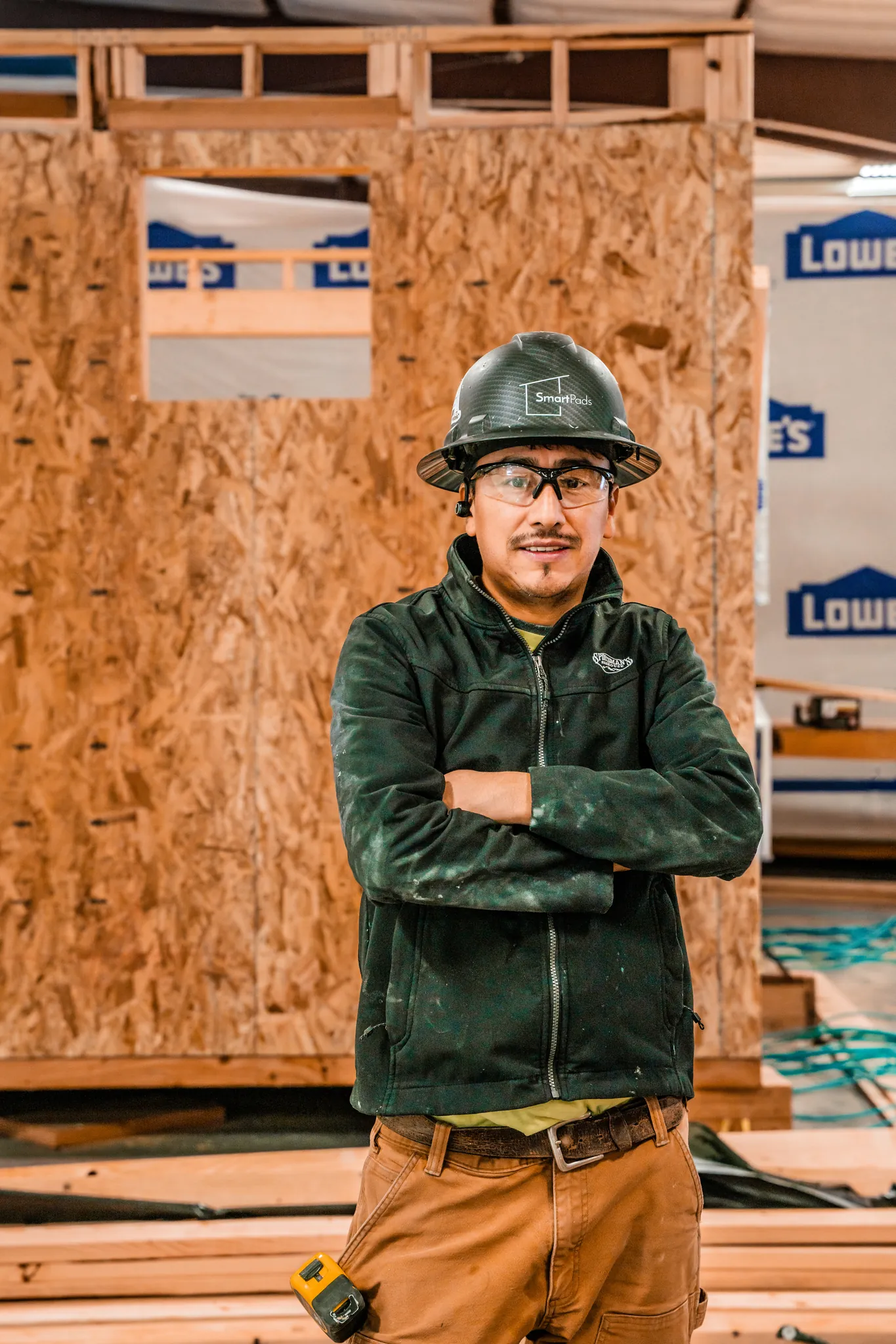 Smartpads worker in hard hat and jacket standing in front of structural building panels in the factory
