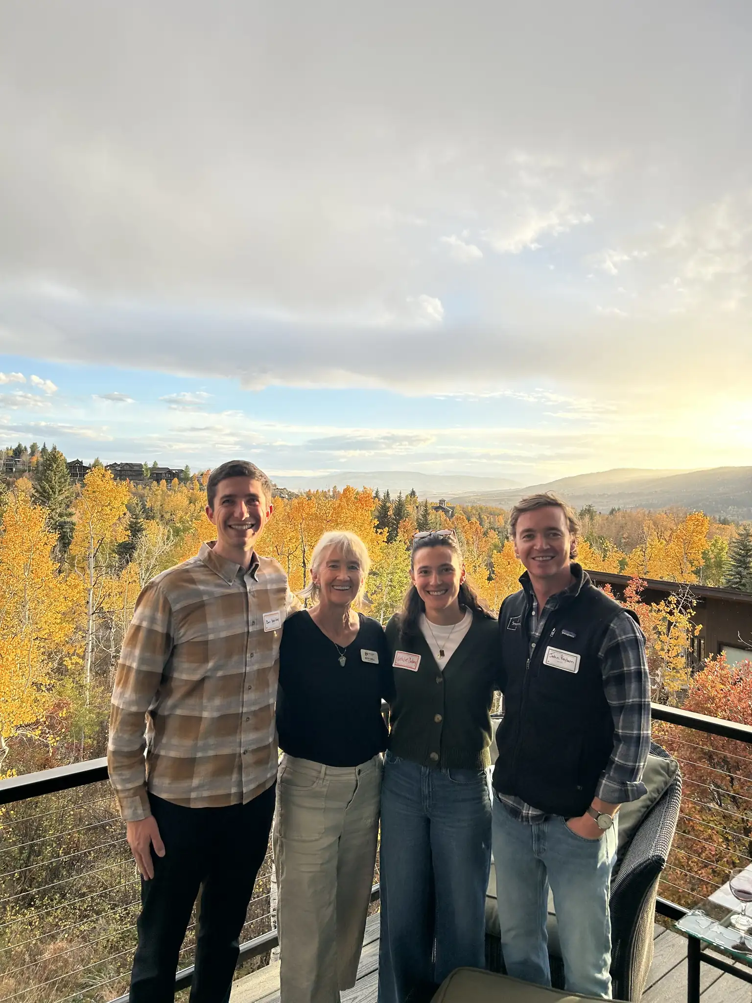 Four people on a deck enjoying a panoramic golden autumn mountain valley view at sunset