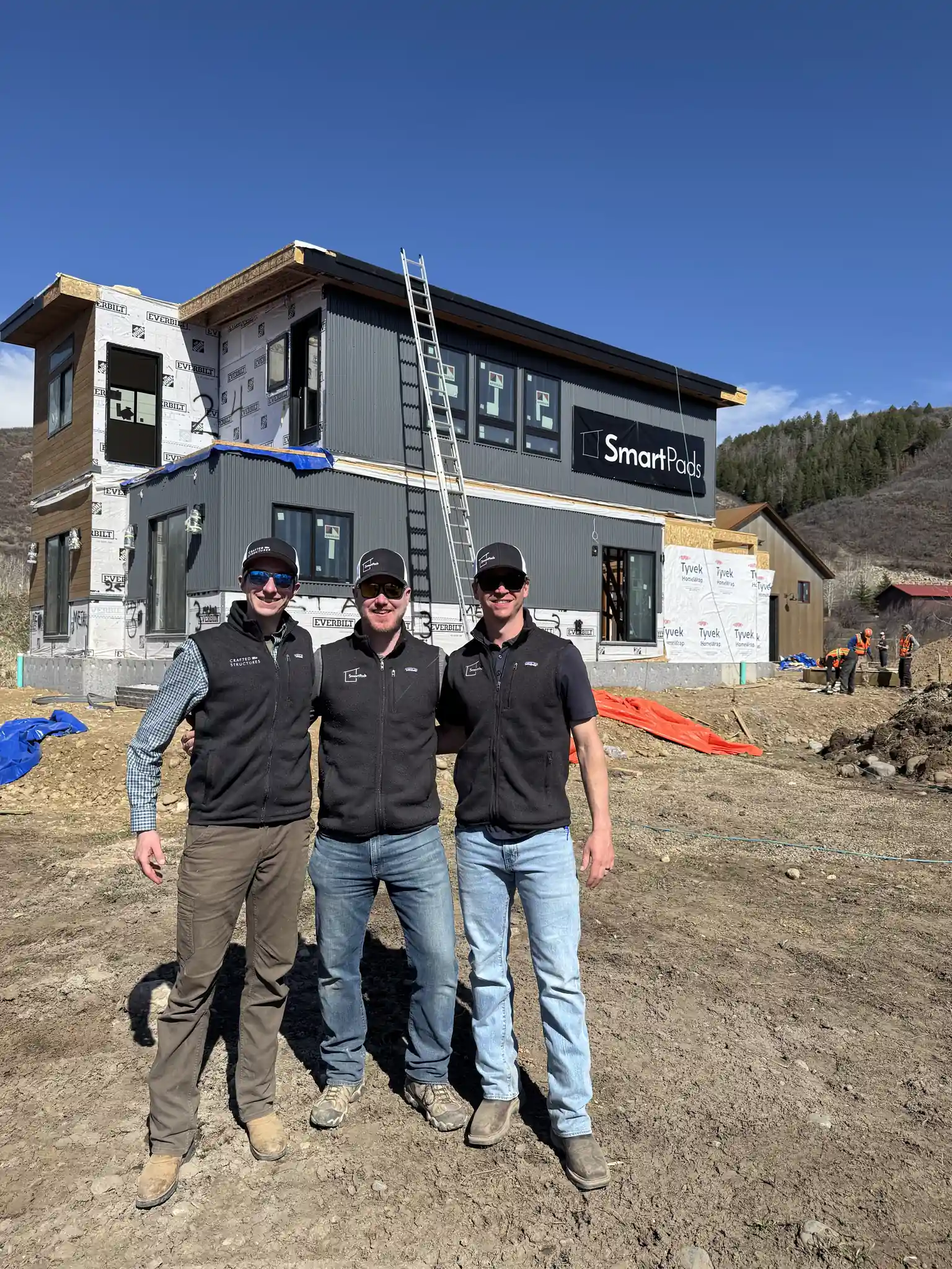 Three Smartpads team members posing in front of a Smartpads modular home under construction