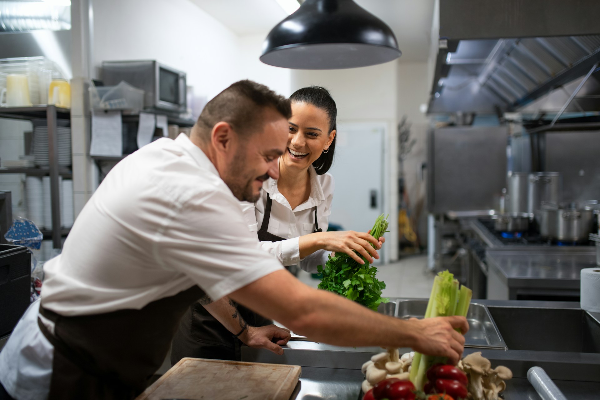 two chefs in restaurant kitchen cutting vegetables and smiling
