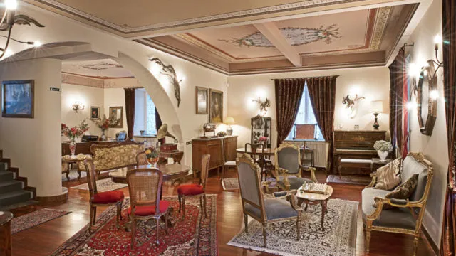 Elegant vintage living room with classic wooden furniture, red and beige rugs, a piano, and floral ceiling artwork.