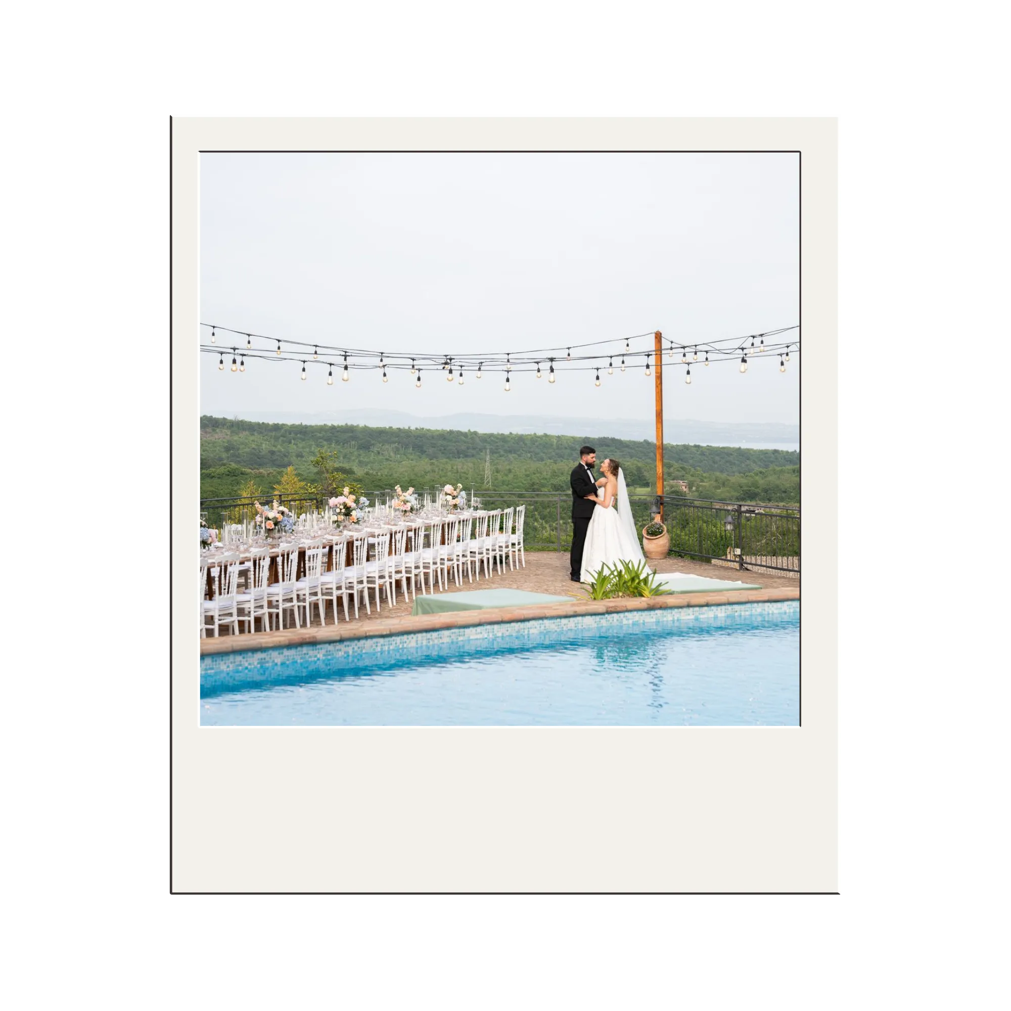 Evening view of a white multi-story villa with lit windows and a swimming pool in the foreground surrounded by greenery.