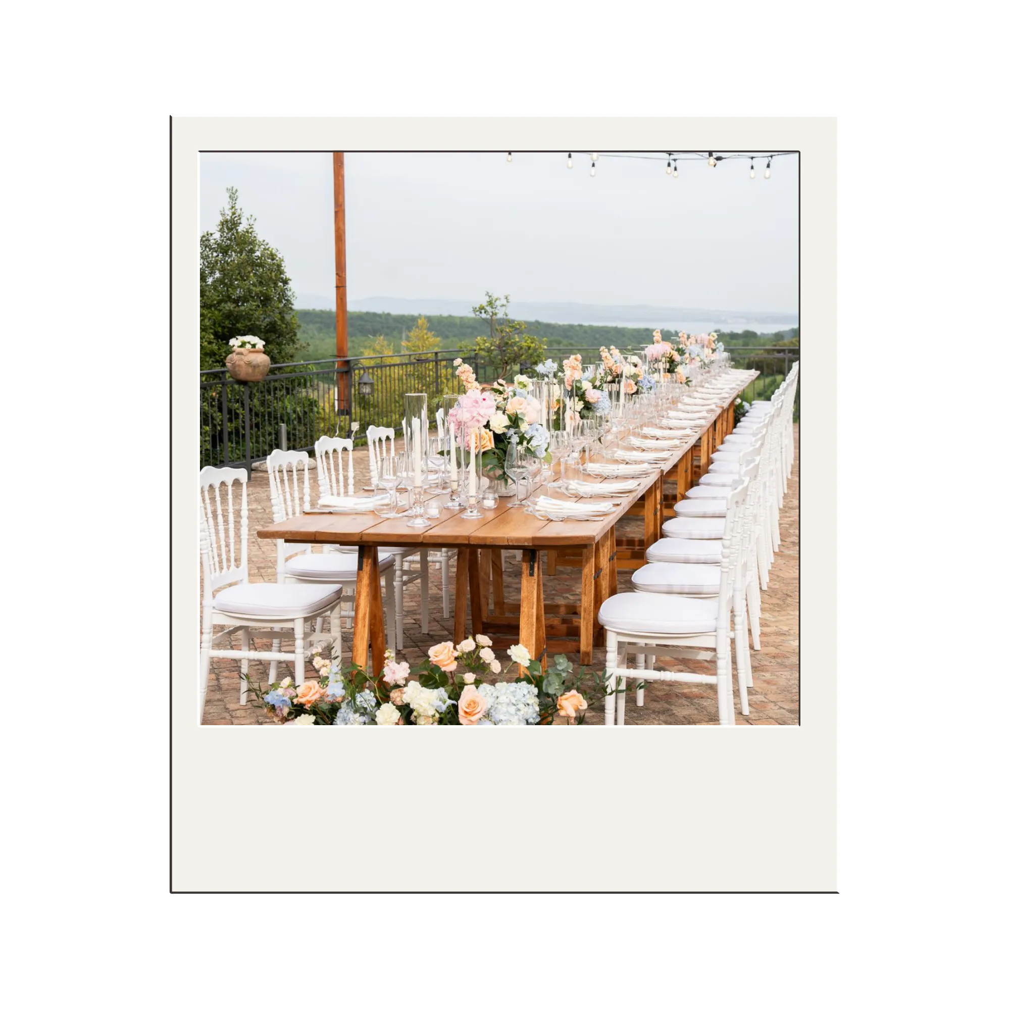 Outdoor wedding ceremony setup with rows of chairs, flower arrangements, string lights, and a person standing at the altar.