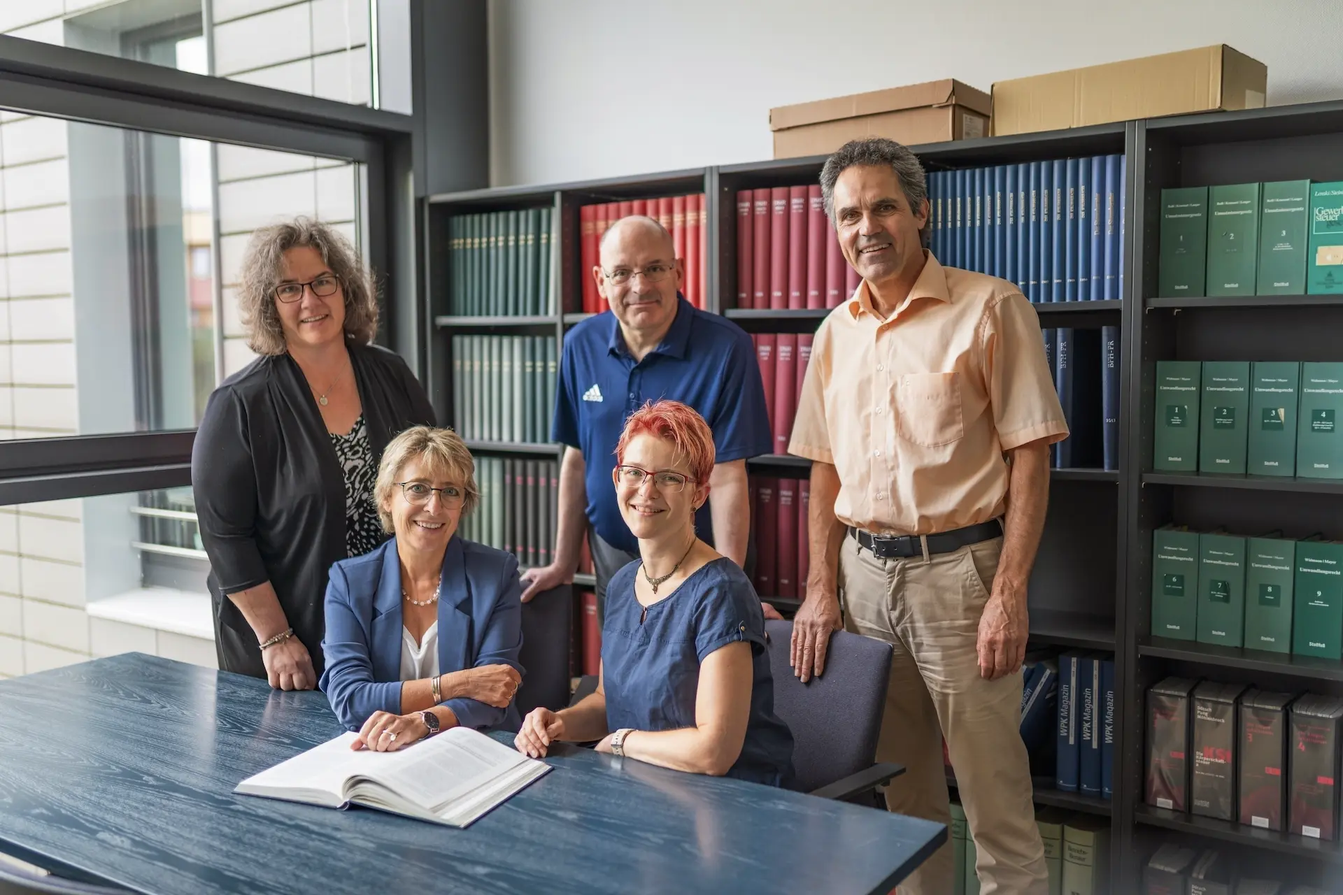 Fünf Mitarbeiter*innen von Schoetz & Partner gemeinsam in der Kanzlei in Göppingen vor einer Fachbibliothek.