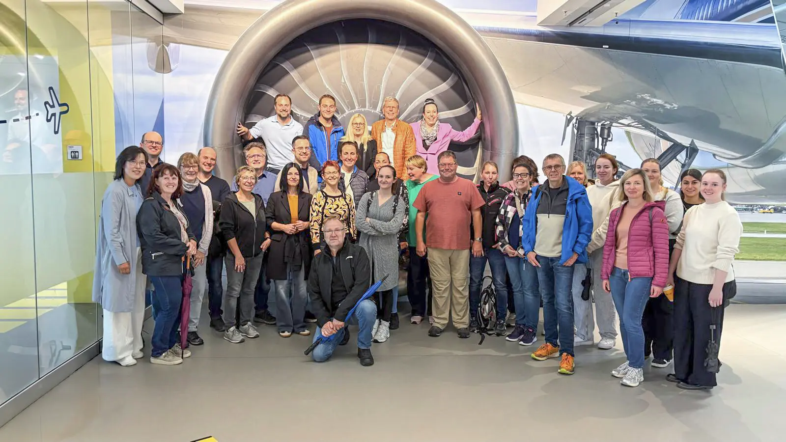 Team von Schoetz & Partner beim Betriebsausflug 2026 vor einem Flugzeugtriebwerk am Flughafen Stuttgart.