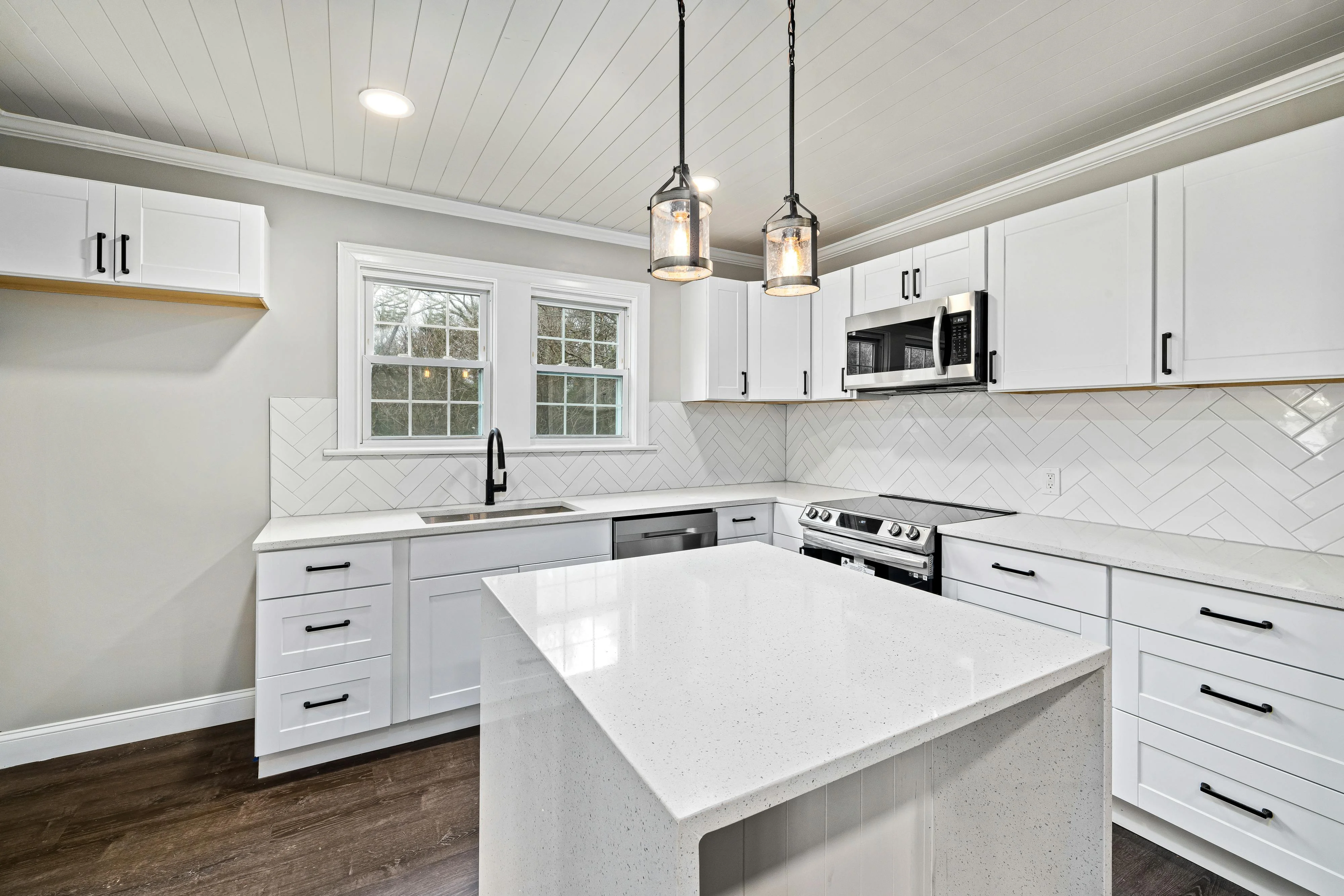 Modern kitchen with white cabinets, a central island, stainless steel appliances, and pendant lights above.