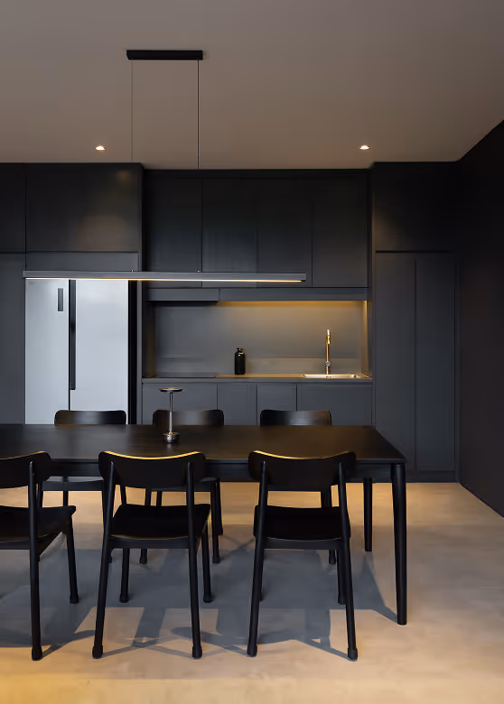 Minimalist modern kitchen with black cabinets, black dining table, six black chairs, and a white refrigerator.