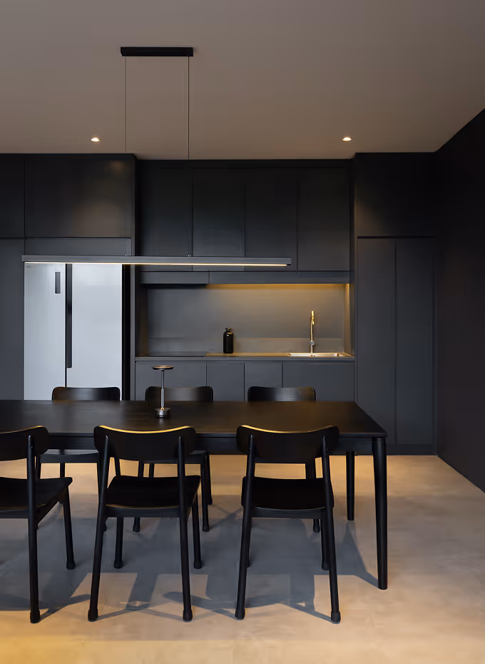 Minimalist modern kitchen with black cabinets, black dining table, six black chairs, and a white refrigerator.