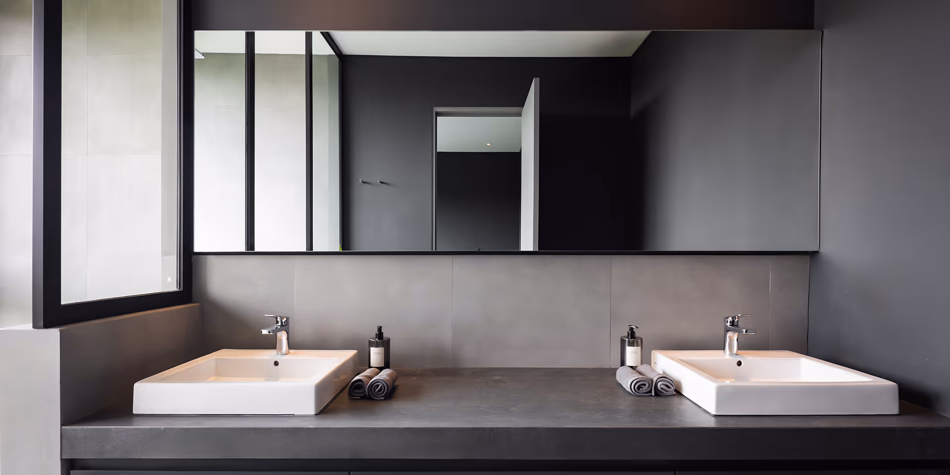 Modern bathroom with two white rectangular sinks, gray countertop, large horizontal mirror, and dark gray walls.