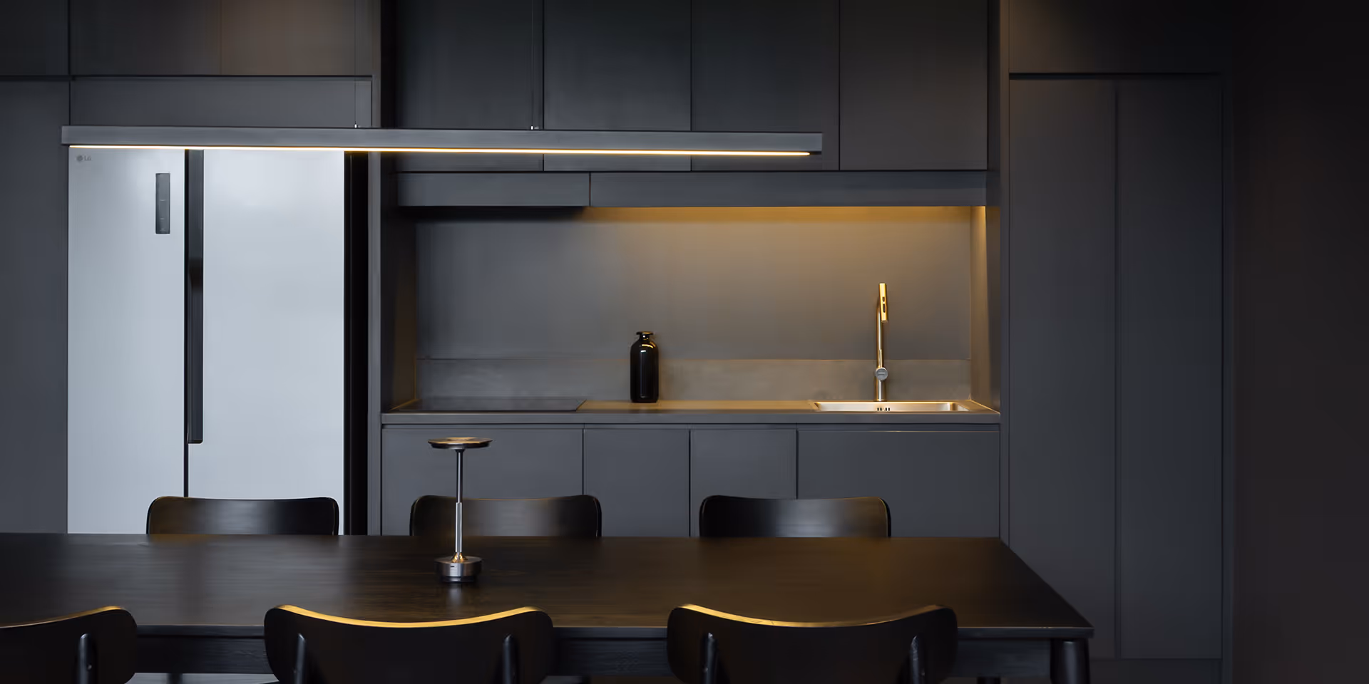 Modern kitchen with dark cabinetry, a white LG refrigerator, a black dining table, and warm under-cabinet lighting.