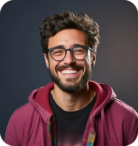 Smiling young man with curly hair, beard, glasses, wearing a maroon jacket and black shirt, against a dark background.