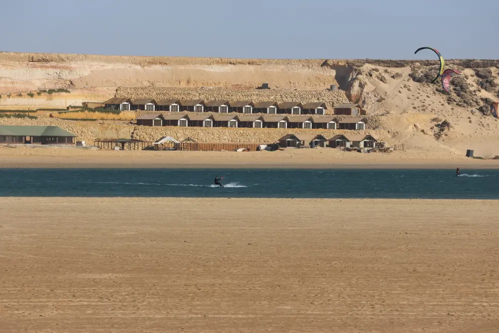 Lagoon-side kitesurfing camp at Dakhla with bungalows below the desert plateau and a rider on the water