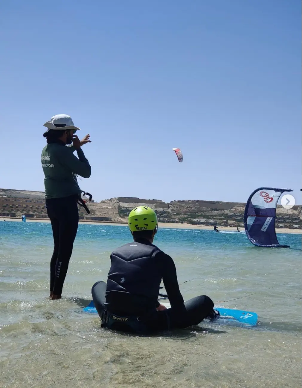 Mirage Dakhla instructor coaching a beginner kitesurfer sitting on a board in the shallow lagoon