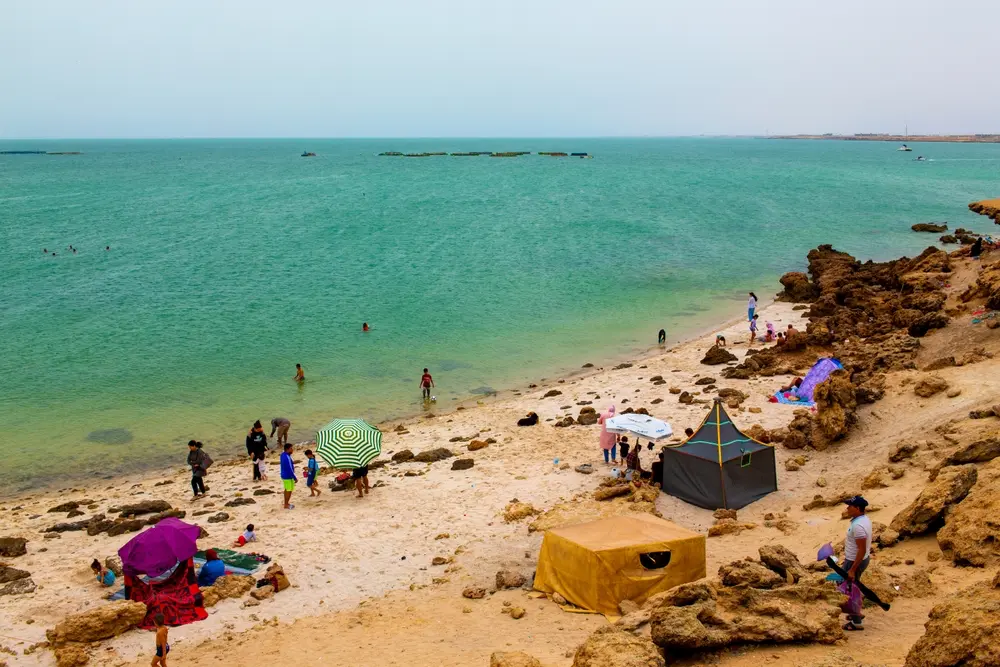 Families relaxing, swimming and sheltering under tents and umbrellas on a rocky beach near Dakhla