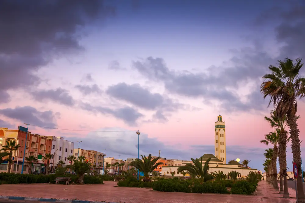 Square in Dakhla at dusk, with a mosque minaret, palms and a pink and purple sky