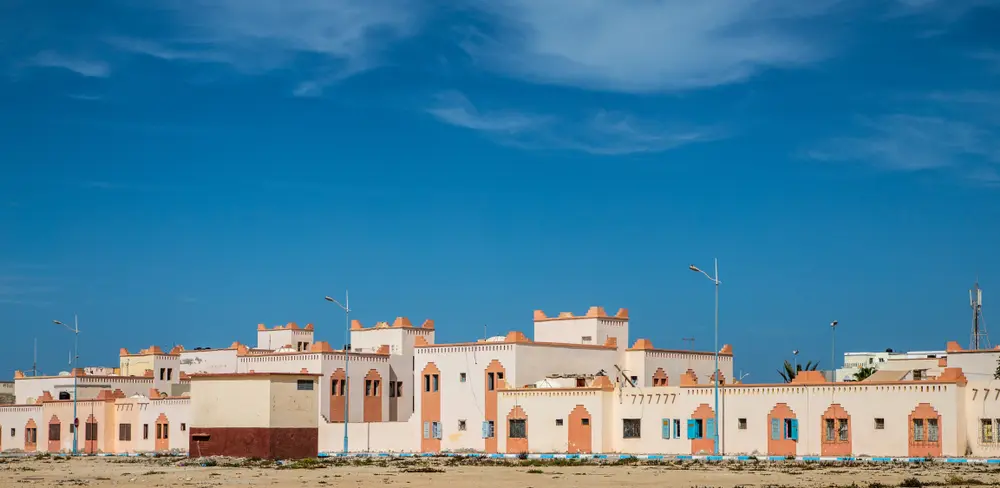 Cream and salmon houses with blue shutters on the edge of Dakhla under a wide cirrus sky
