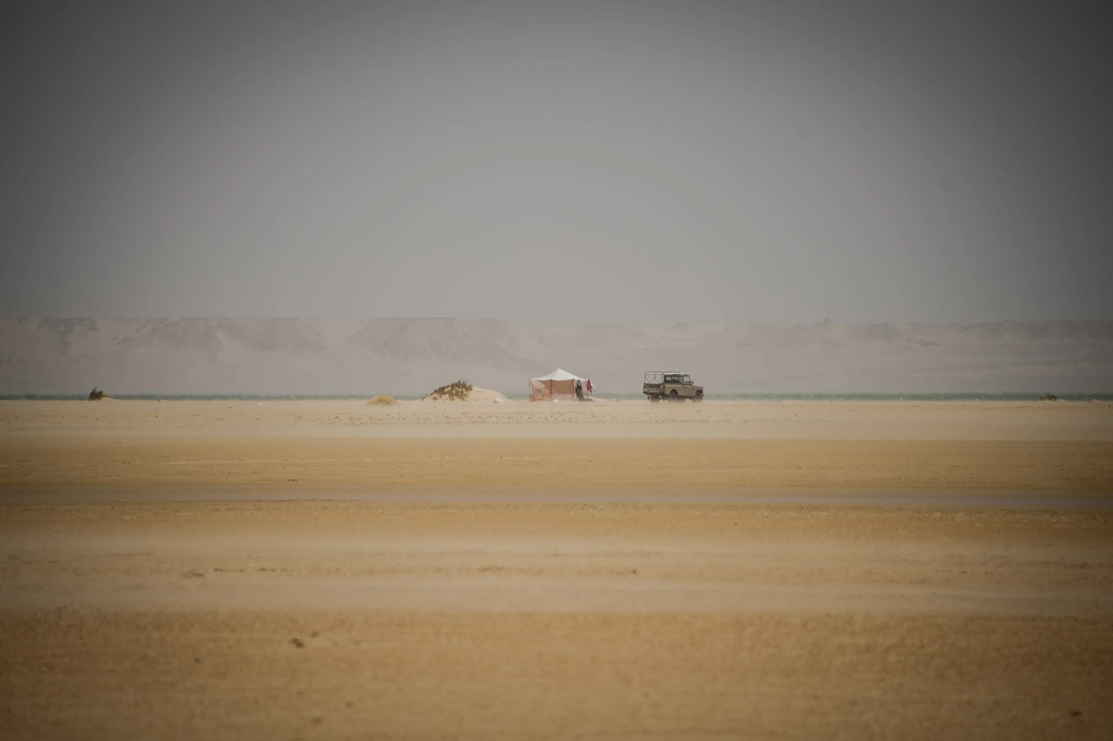 Empty sand flats on the lower Dakhla lagoon at low tide, a 4x4 and camp tents small on the horizon