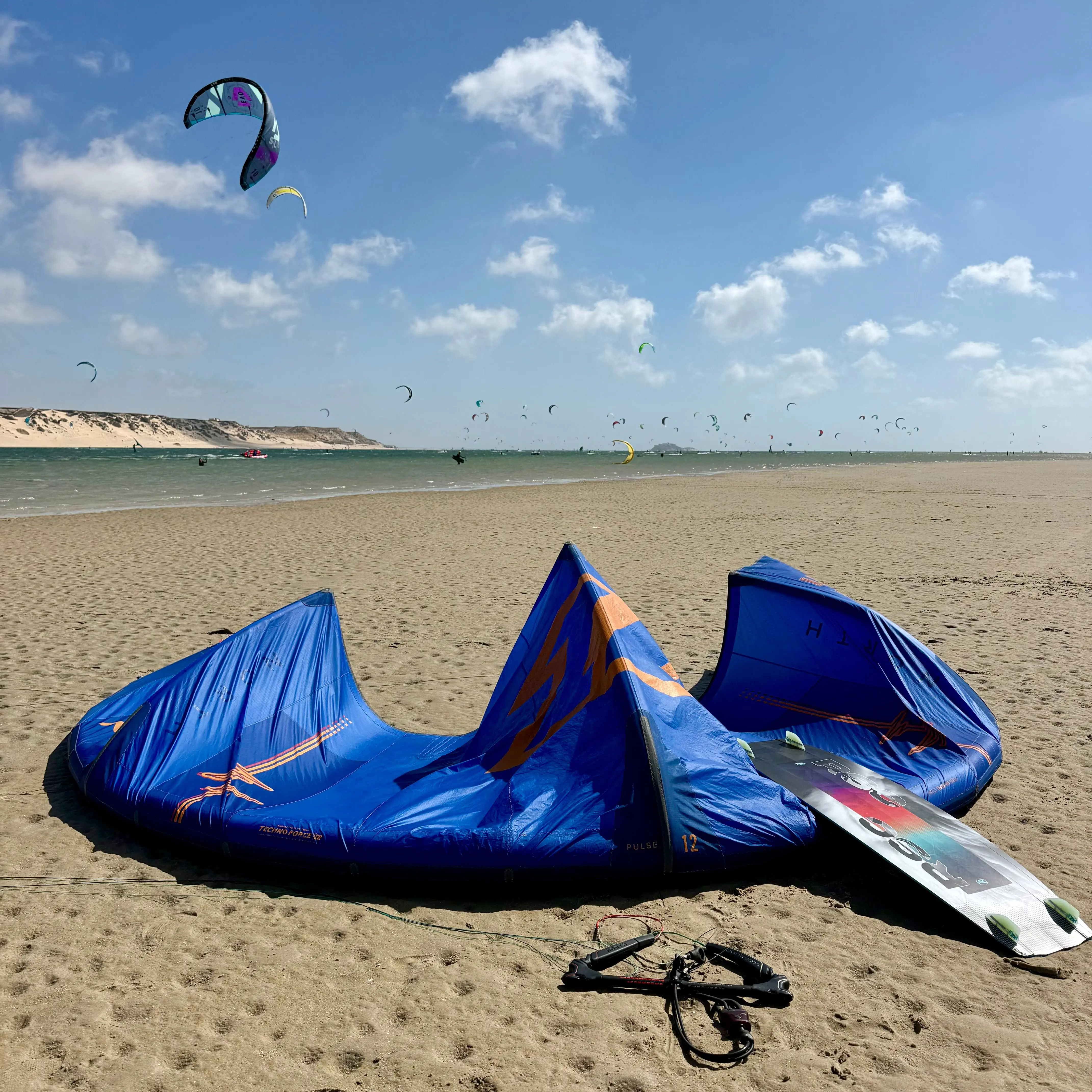 Kite and board rigged on the sand at low tide on the Dakhla lagoon, kites flying above the water behind