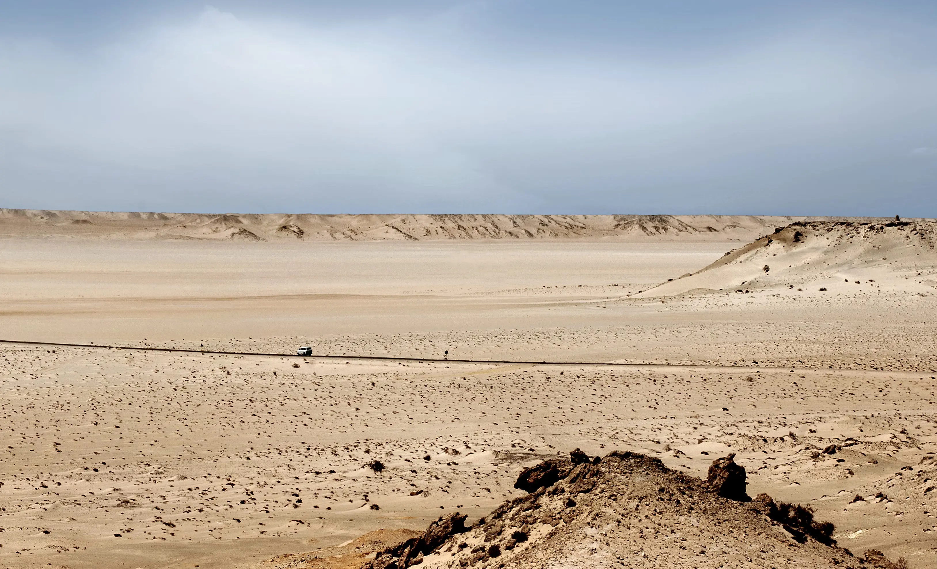 A lone 4x4 on a track across the flat Dakhla desert, with a low dune ridge along the horizon