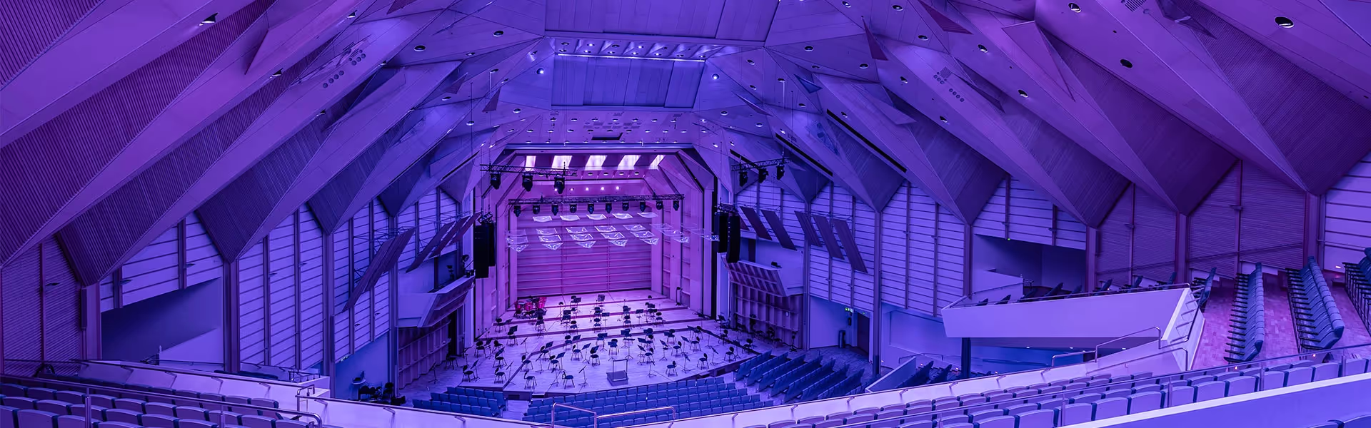 Picture of a stage with chairs, music stands and several rows of benches for the audience in a large concert hall.