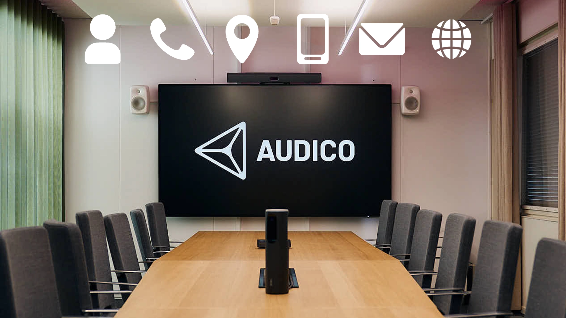 Conference room with a large table, several chairs and a large screen and speakers.