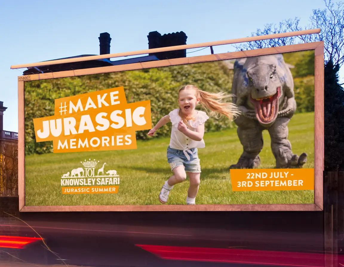 Billboard showing a young girl running on grass with a roaring dinosaur behind her, promoting Knowsley Safari Jurassic Summer event from 22nd July to 3rd September.