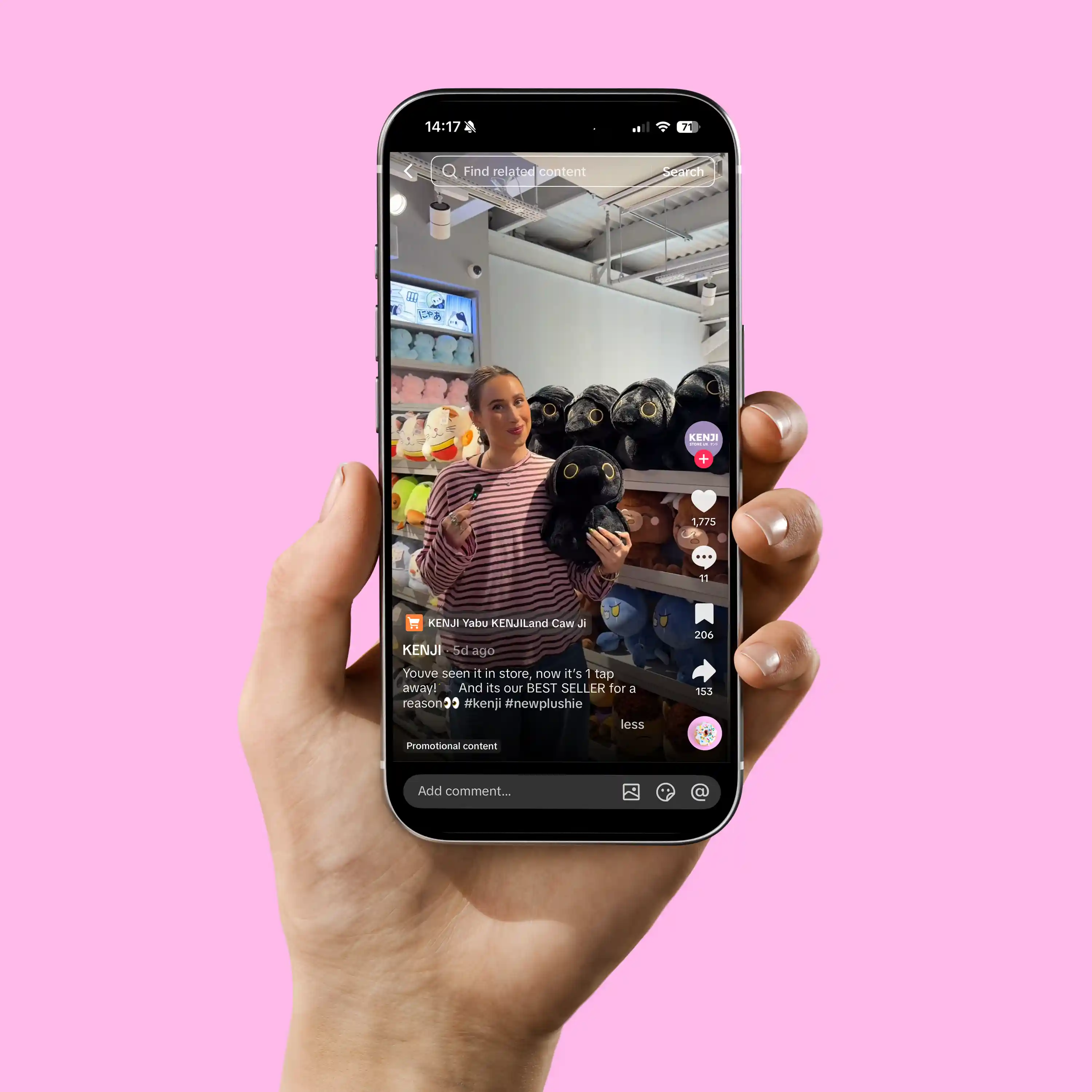 Hand holding phone displaying a woman in a shop holding a black plush toy with shelves of colorful toys behind her.
