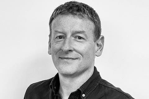 Black and white portrait of a man with short hair wearing a dark buttoned shirt, smiling slightly.