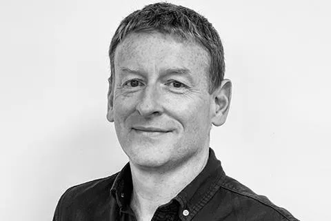 Black and white portrait of a man with short hair wearing a dark buttoned shirt, smiling slightly.