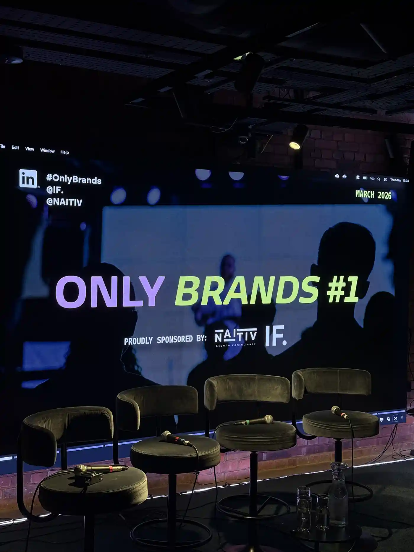 Empty stage with four microphones on chairs in front of a screen showing ONLY BRANDS #1 event signage.