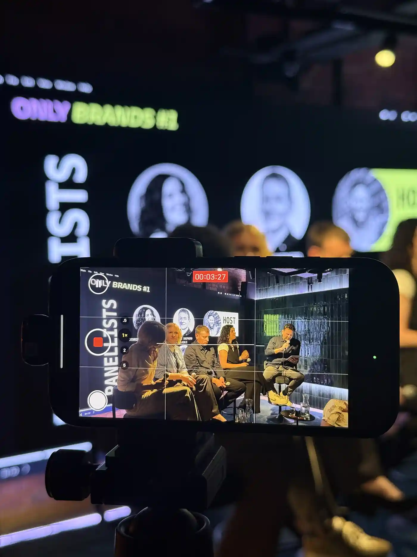 Smartphone recording a panel discussion with five people seated on a stage.