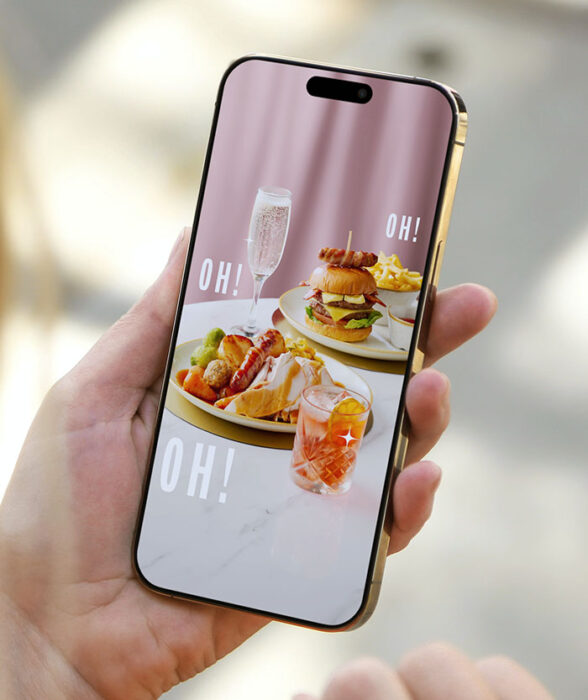 Hand holding a smartphone displaying a photo of a burger, fries, roast dinner, and two drinks with text OH!