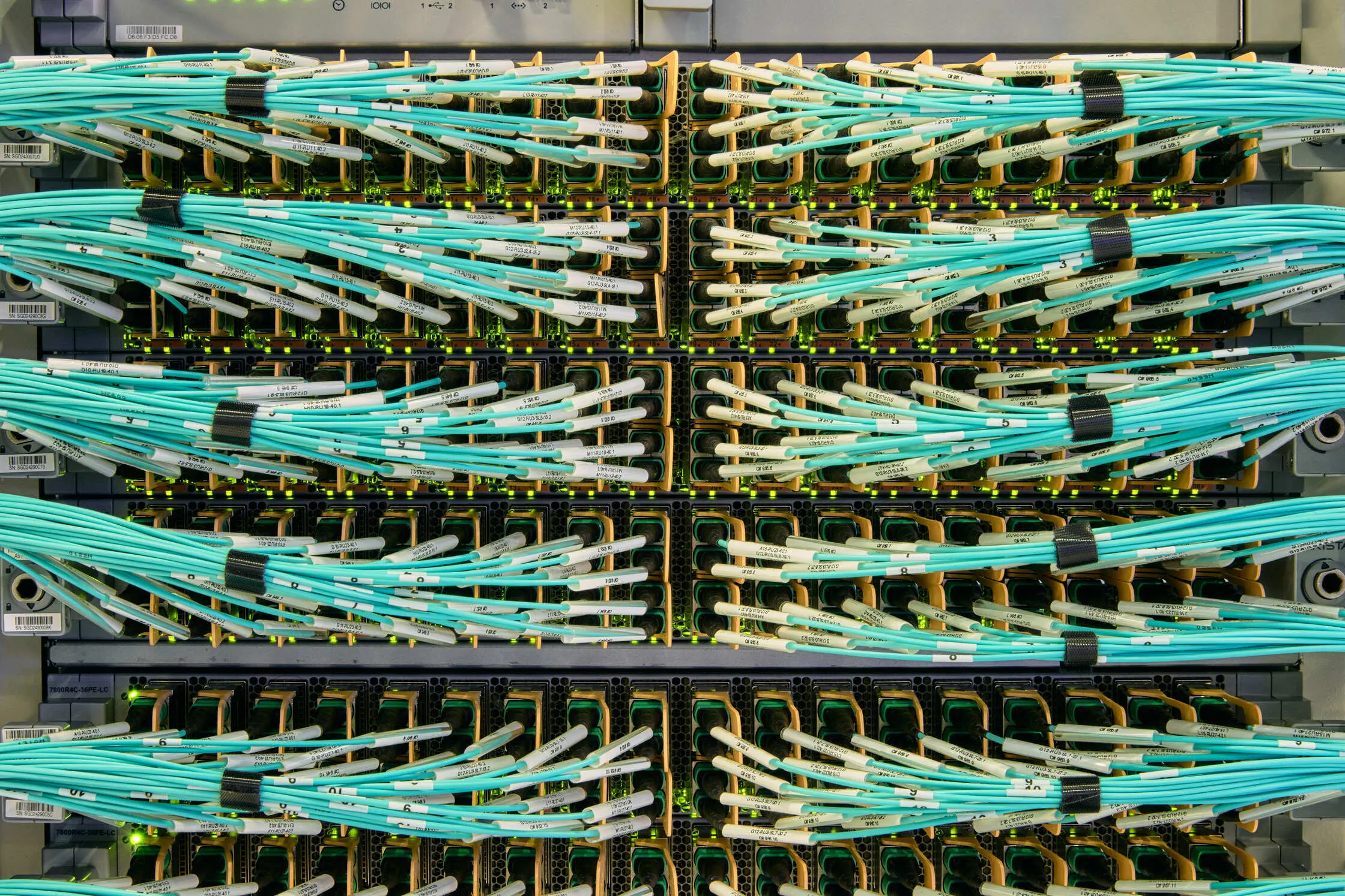 Rows of teal fiber optic cables patched into network switches in a TeraWulf data center.