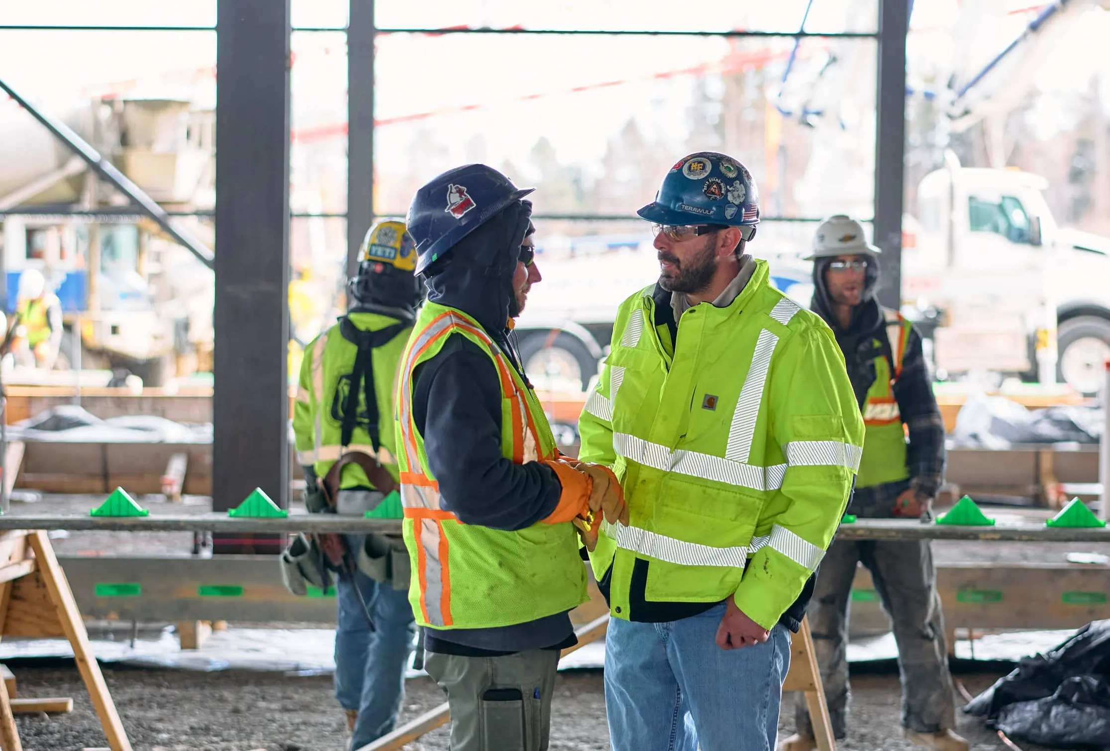 Two TeraWulf construction workers in hi-vis jackets talking on the Lake Mariner data center job site.