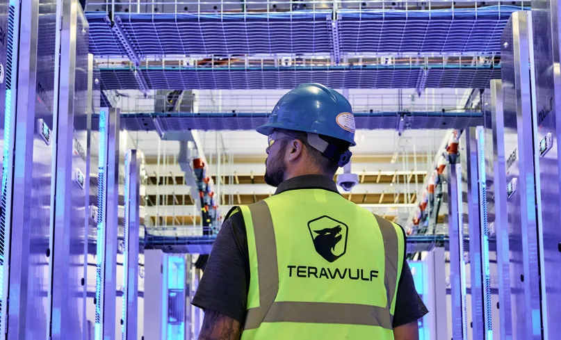 TeraWulf technician in branded safety vest and hard hat inside a Lake Mariner data hall.
