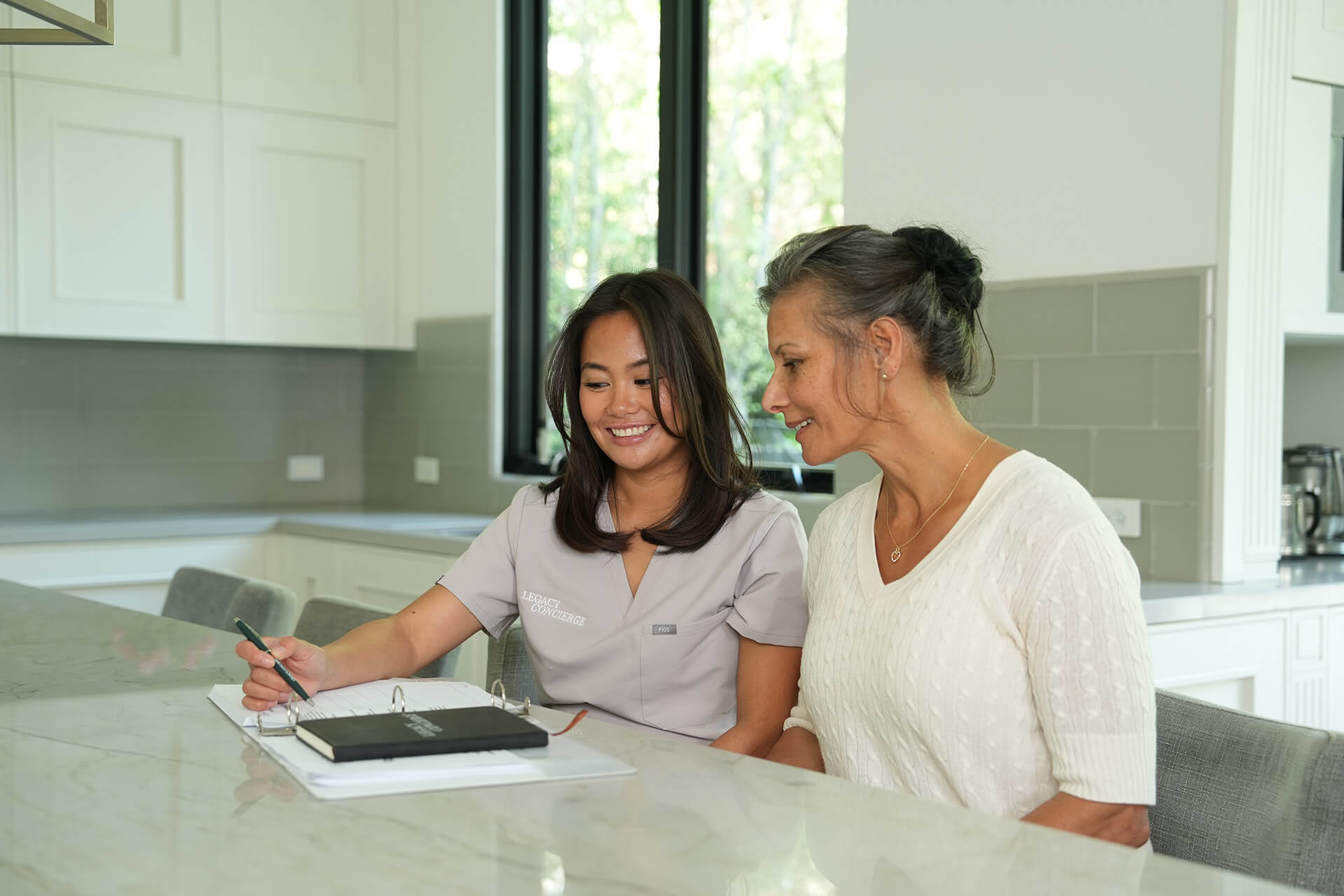 Two women at a table, one is showing the other a document.