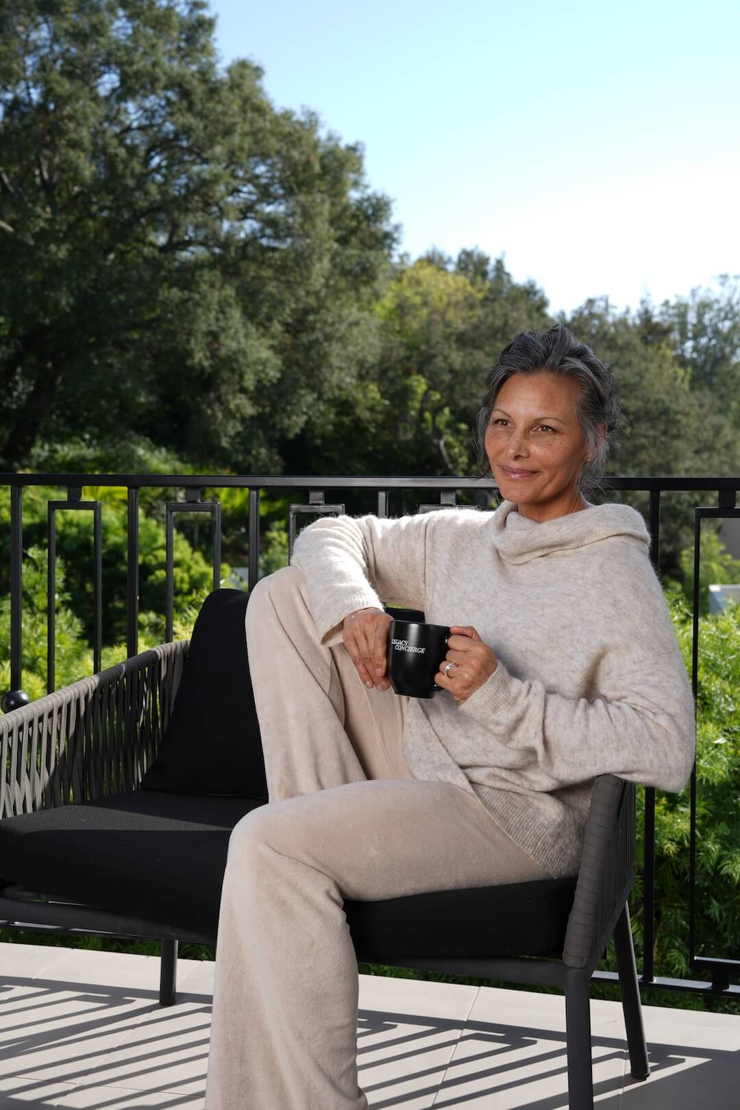 Woman sitting on a bench in a garden with a cup of coffee in her hand.