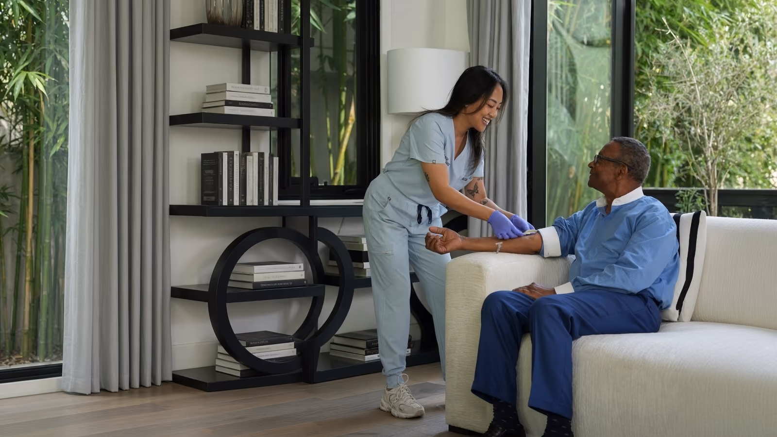 Woman administering an IV to a man in his home sitting on a couch.